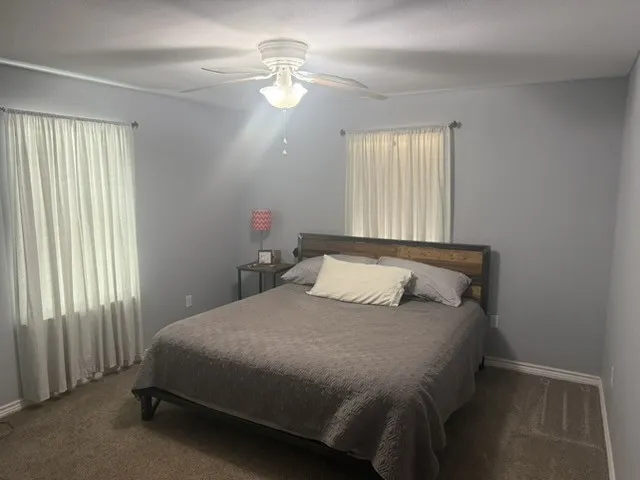 Barndominium - Carpeted bedroom with a ceiling fan light fixture and dual windows.
