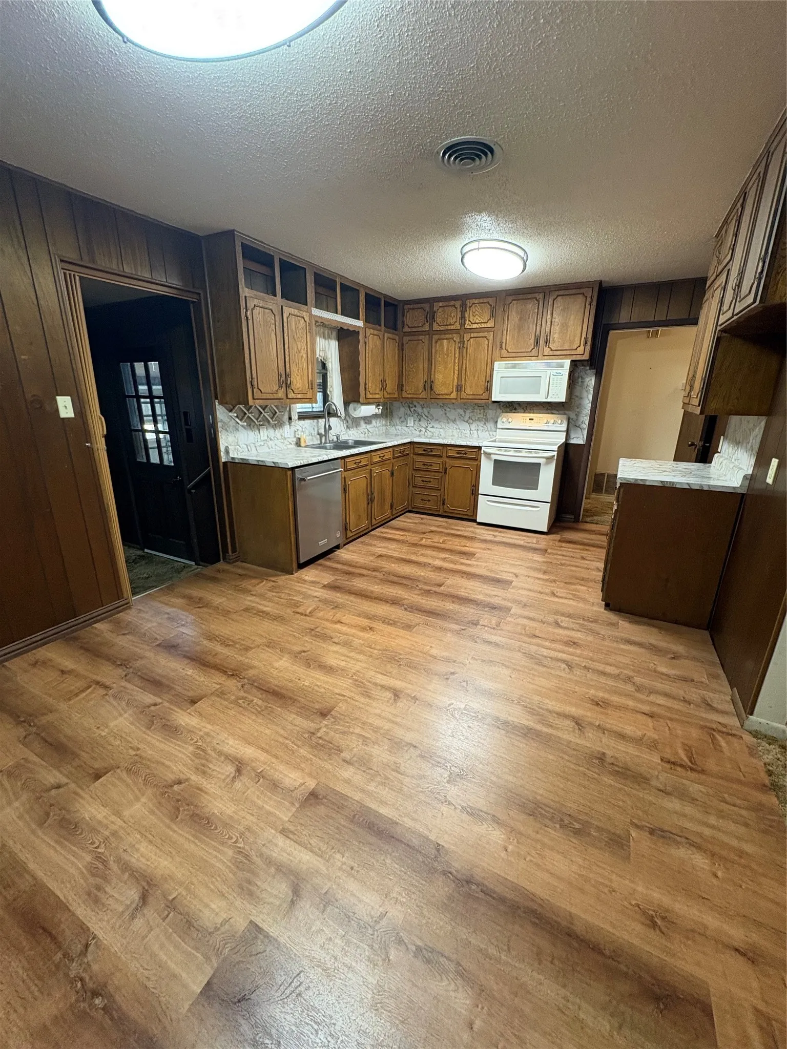 Kitchen featuring wood-finish flooring, wood cabinetry, white tile backsplash, and white appliances