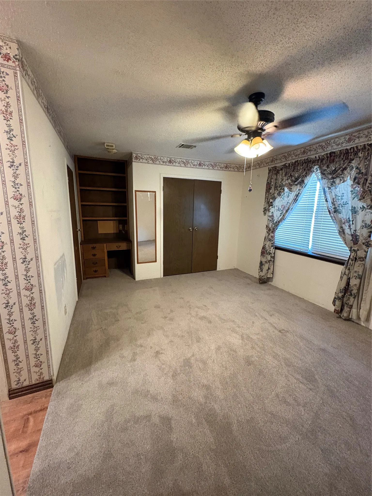 Room featuring a ceiling fan with integrated lighting, built-in wooden shelving, a built-in wooden desk, and a window with blinds.
