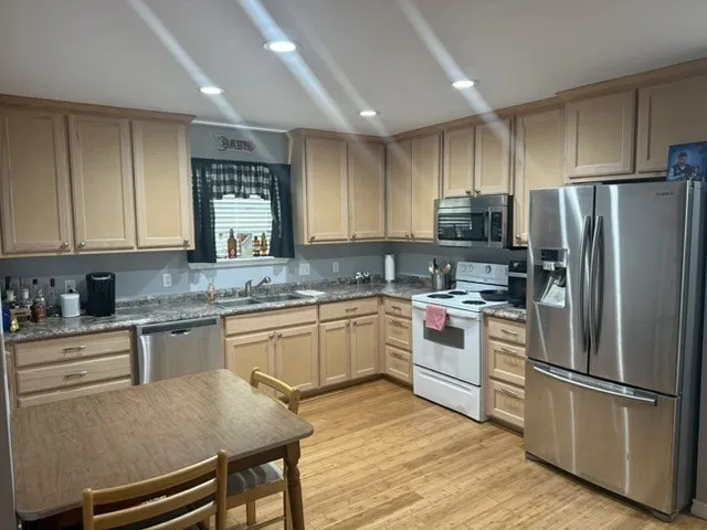 Barndominium - Kitchen with recessed lighting, wood-finish flooring, wood-finish cabinetry, stainless steel dishwasher, and stainless steel refrigerator.