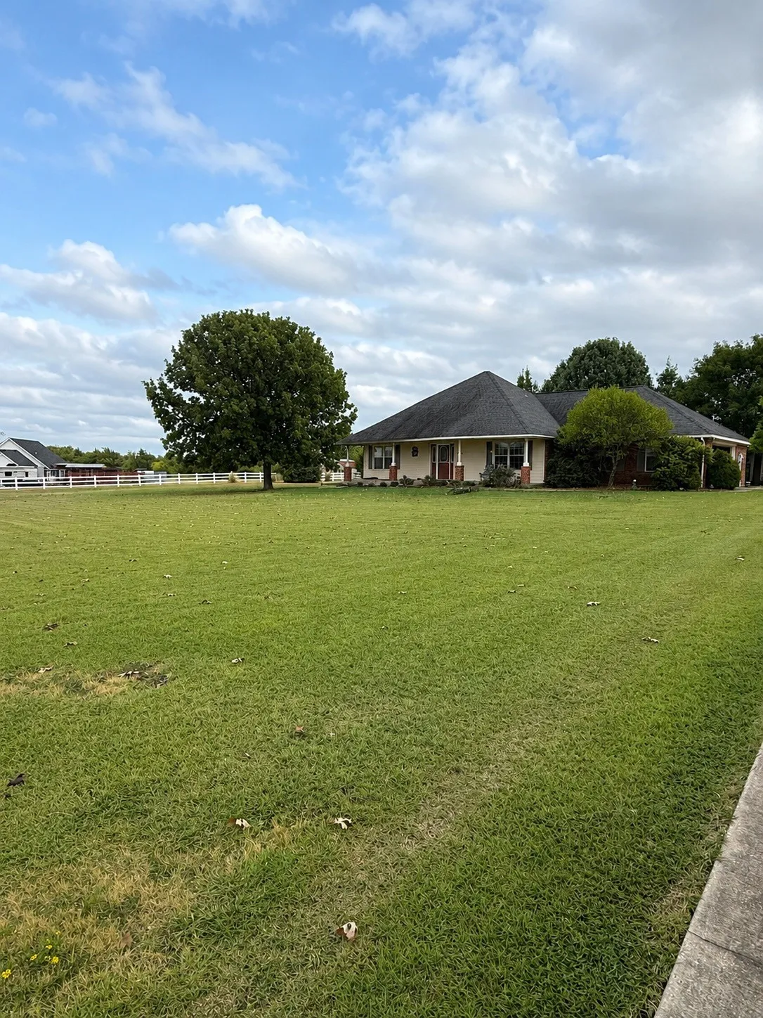 Expansive grounds featuring mature landscaping and manicured lawn, with a single-story residence showcasing a traditional architectural style, pitched roofline, and brick exterior set back from the property line