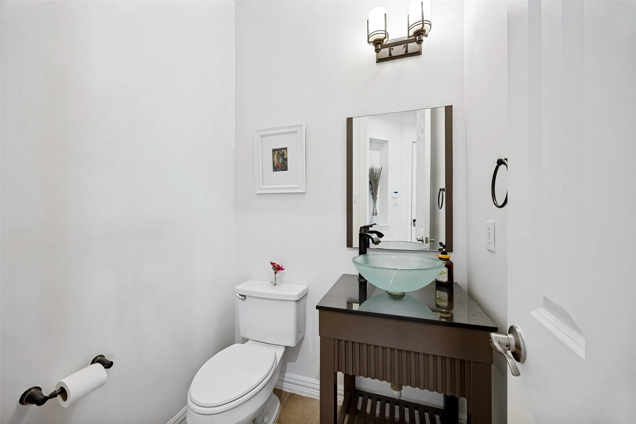 Vessel sink with a dark wood-finish vanity, wall-mounted light fixture, and a framed mirror