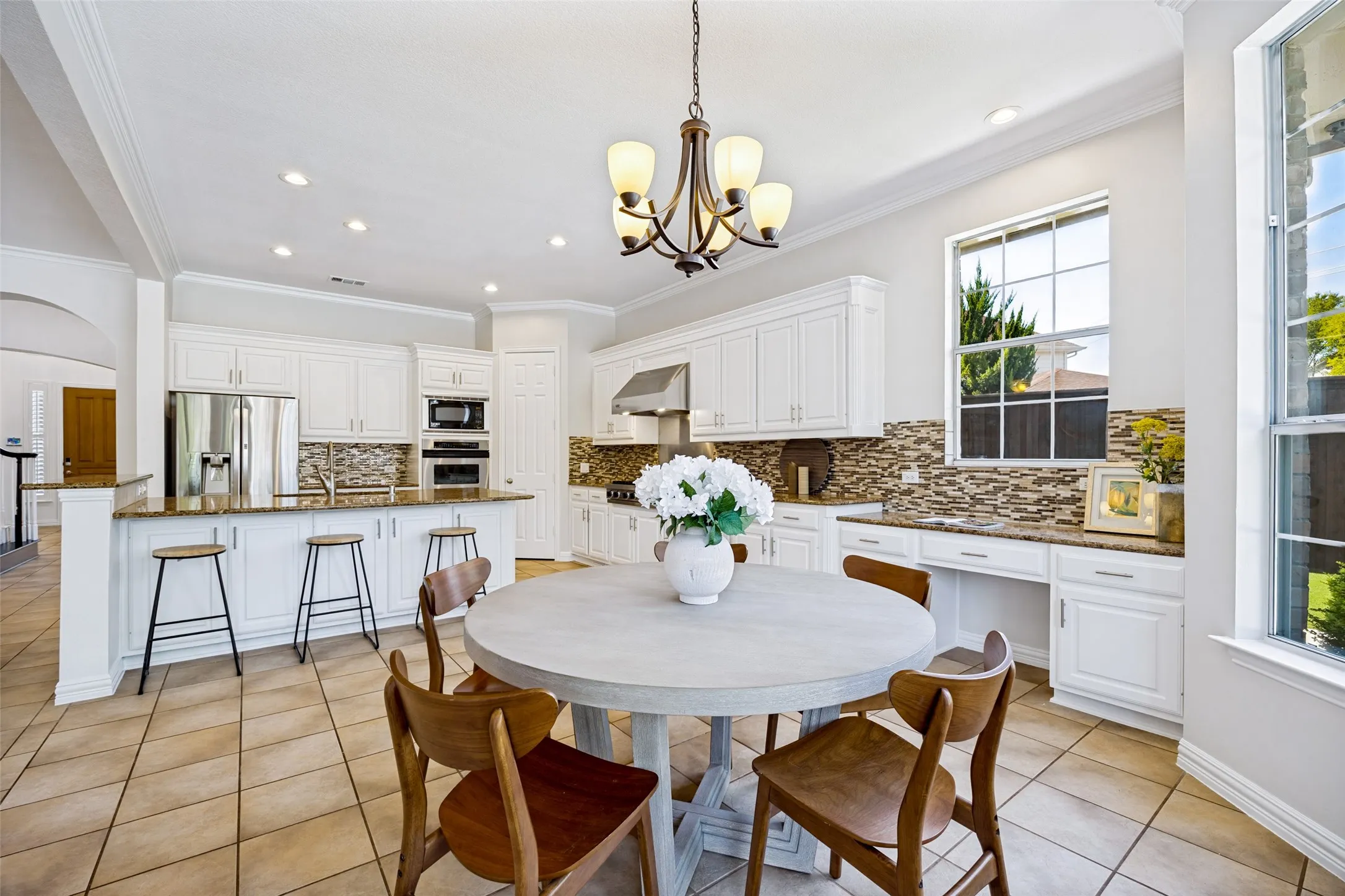 Bright kitchen featuring white cabinetry, stainless steel appliances, viking rangetop, a mosaic tile backsplash, a kitchen island with seating, and tile flooring