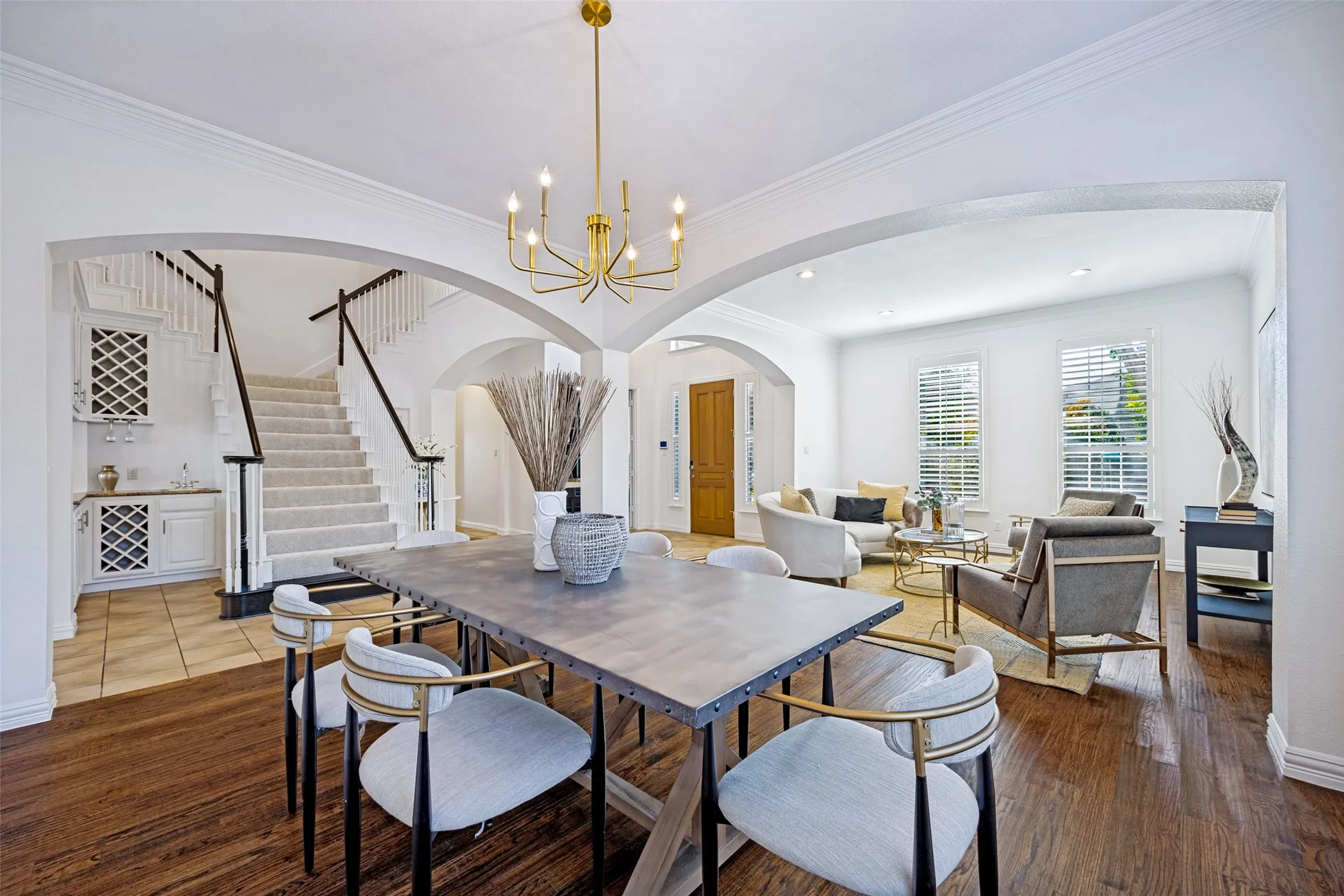 Hardwood flooring, arched doorways, a built-in wet bar, a carpeted staircase with dark wood railings, and a gold-tone chandelier
