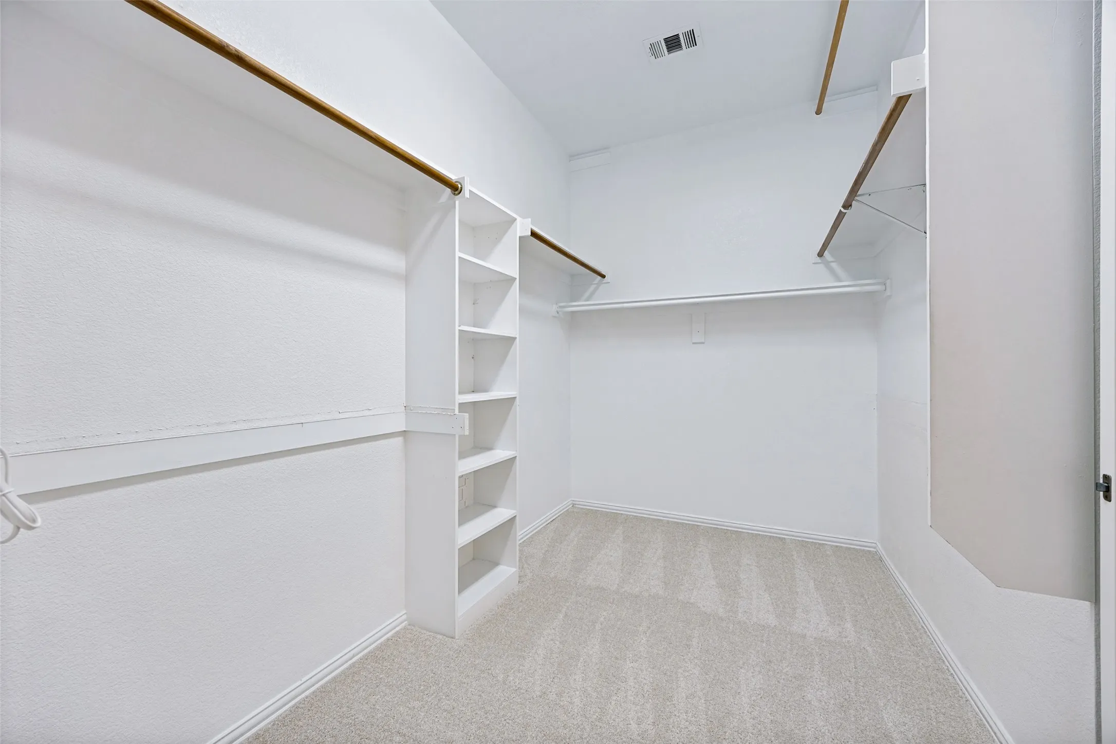 Neutral tone wall paint, light-colored carpeting, multiple clothing rods, built-in shelving, and white trim