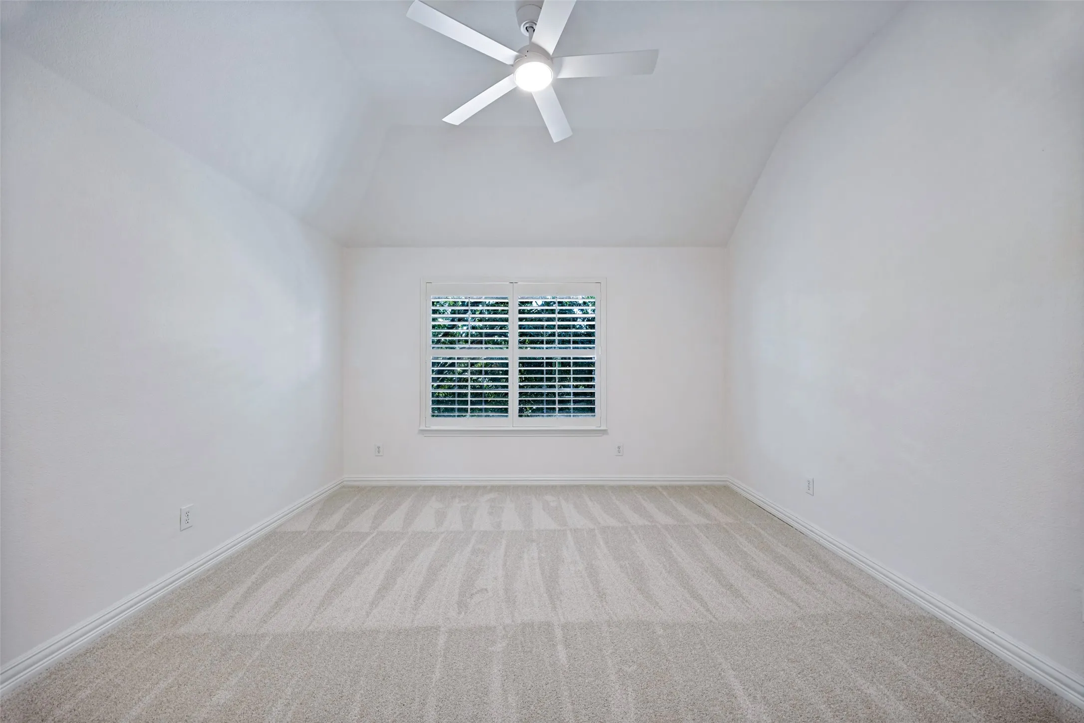 Vaulted ceiling with a ceiling fan, window with plantation shutters, and light-toned carpet