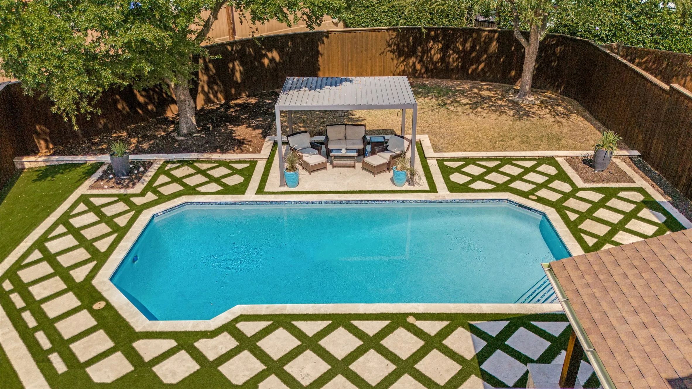 Geometric inground pool surrounded by patterned stone and artificial turf