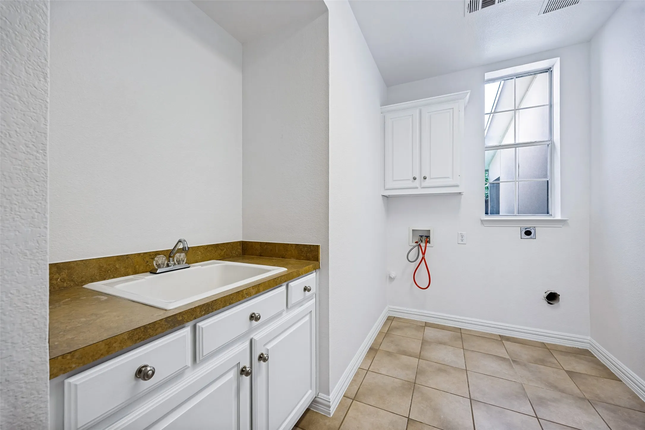 Utility room with a built-in sink, white cabinetry, and tiled flooring w room for an extra fridge or freezer