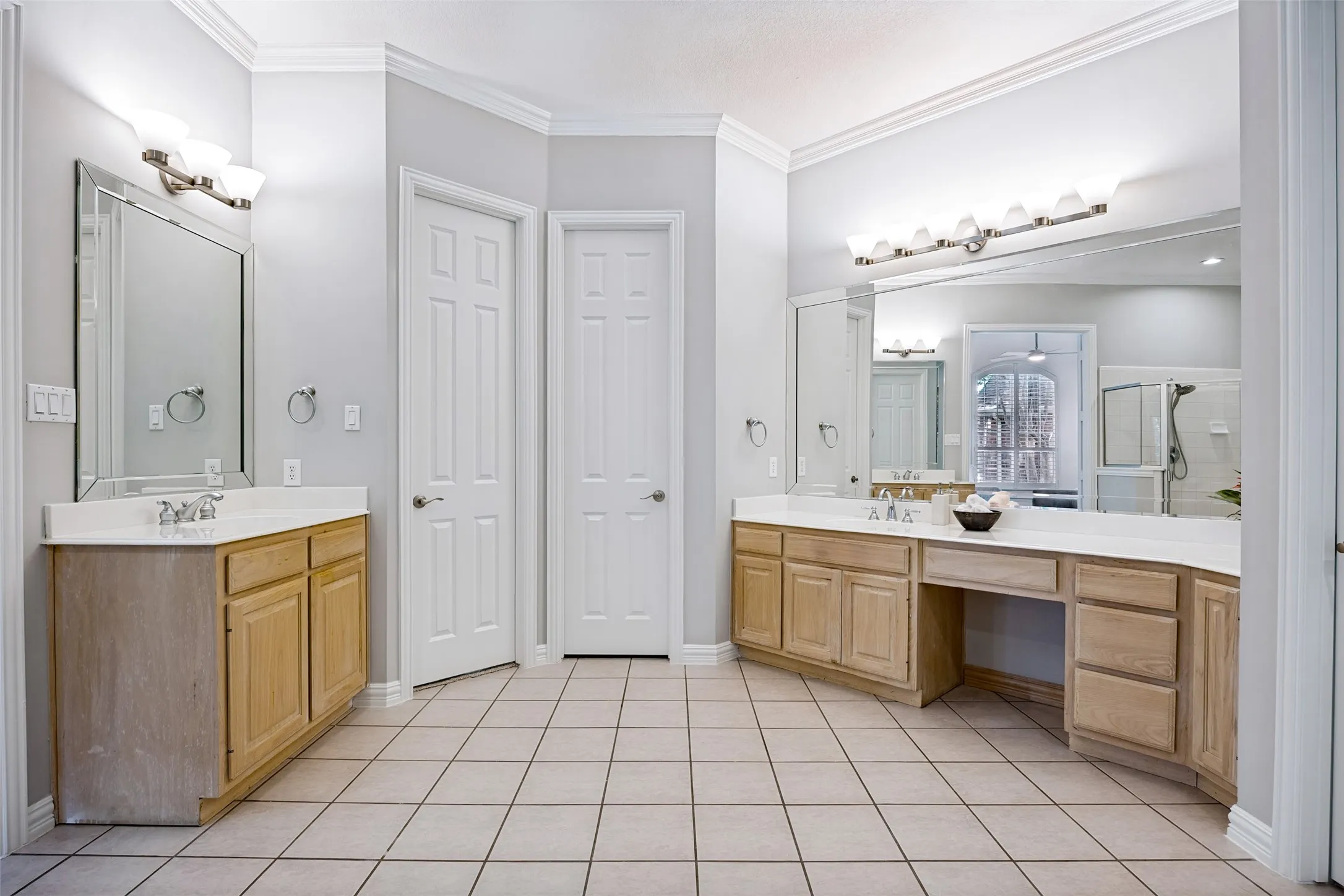 Dual wood-finish vanities with integrated sinks and white countertops, large wall-mounted mirrors, and tiled flooring