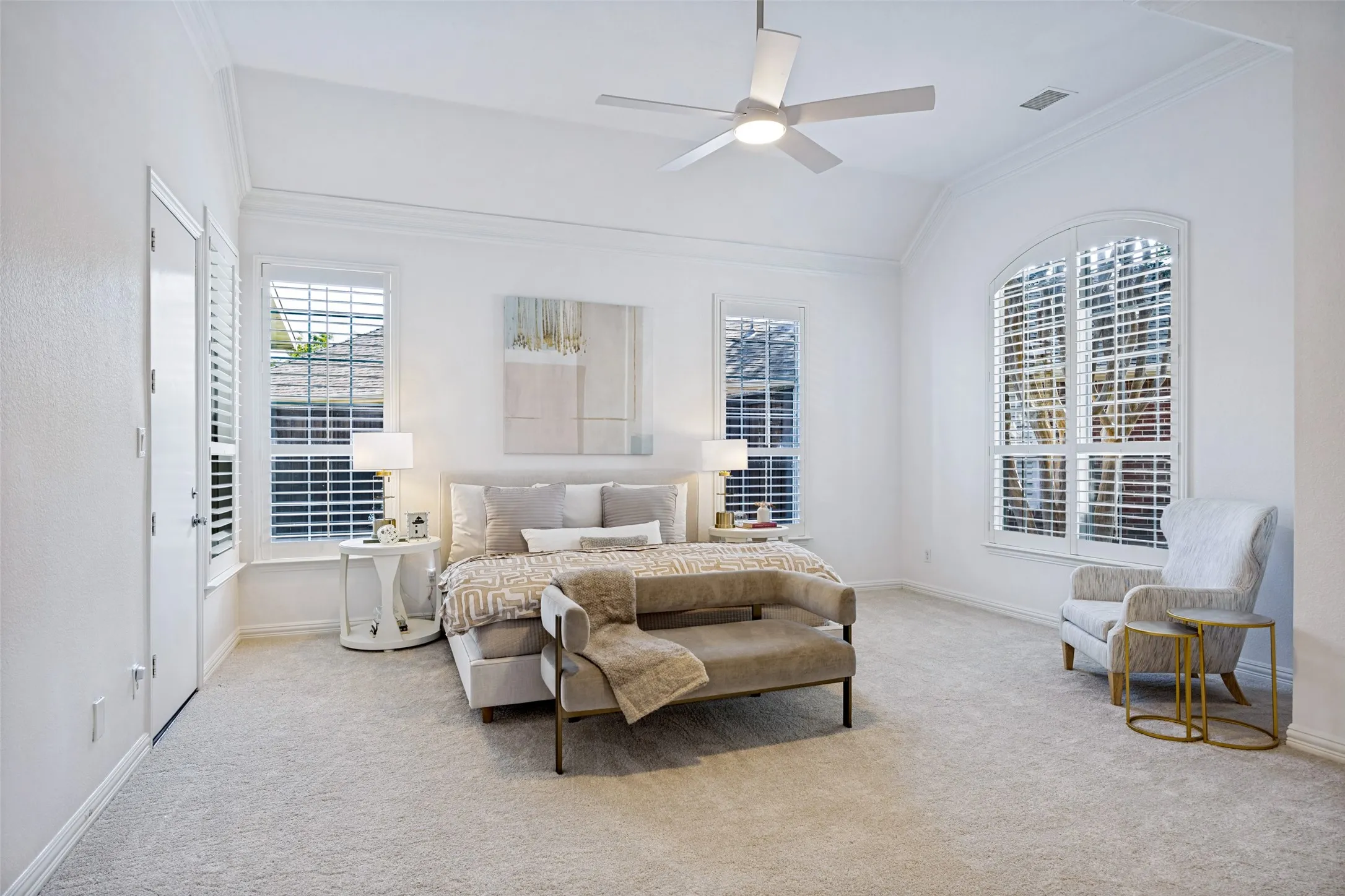 Vaulted ceiling with crown molding, ceiling fan, arched window, and two additional windows with plantation shutters and new carpet