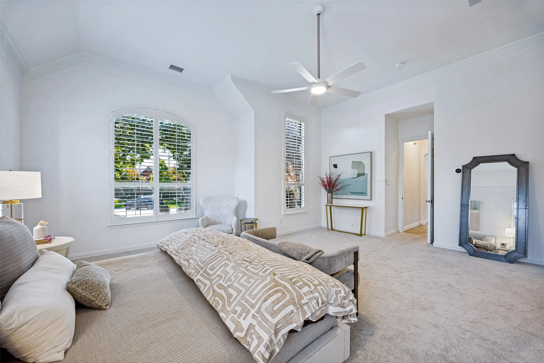 Arched window with plantation shutters, vaulted ceiling, crown molding, ceiling fan with integrated lighting, and carpeted flooring