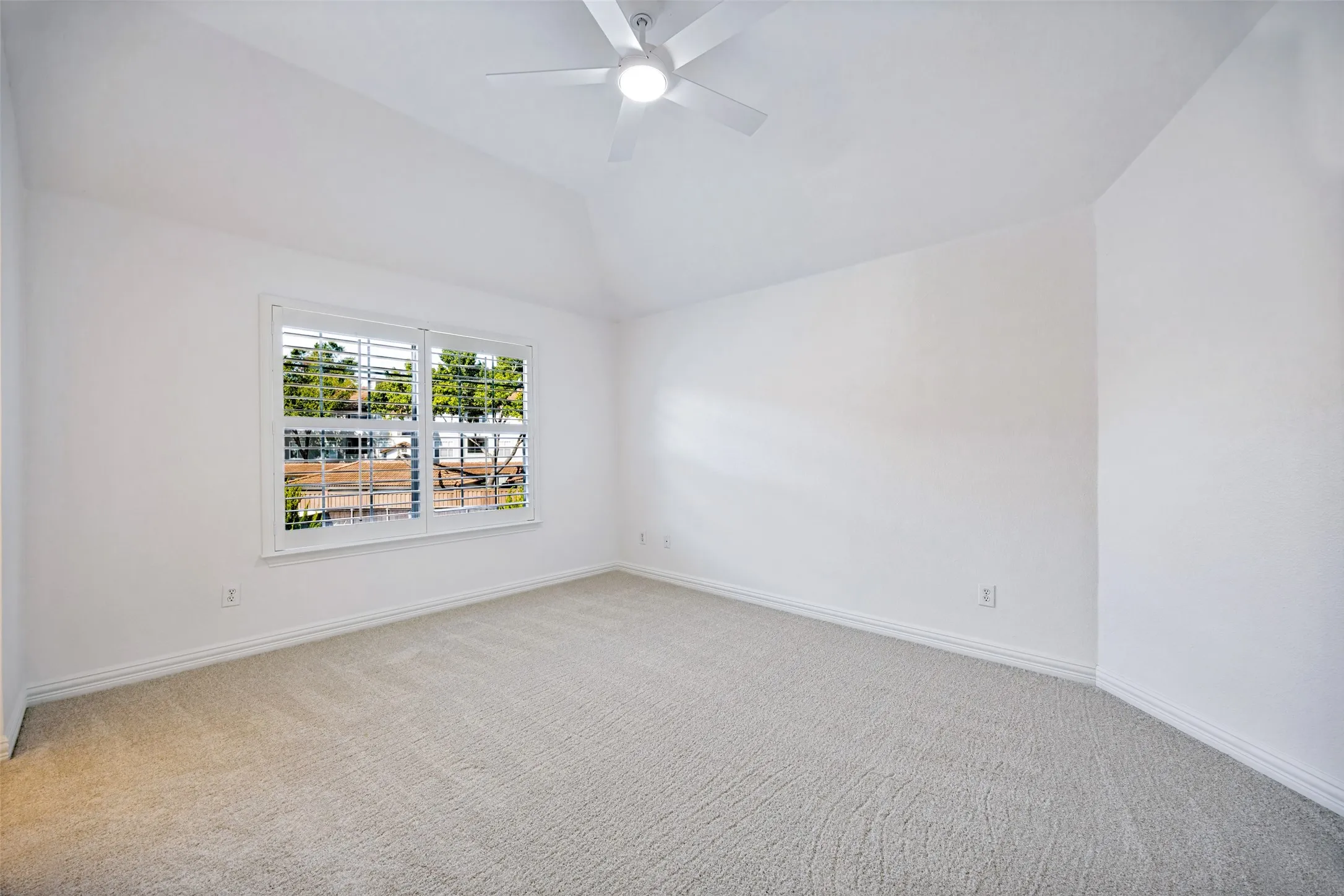 Vaulted ceiling, ceiling fan, carpet flooring, window with plantation shutters, white wall finishes