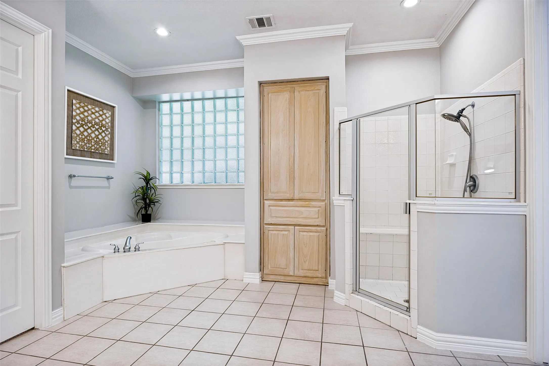 Corner soaking tub with deck-mounted faucet, glass block window, and tile flooring