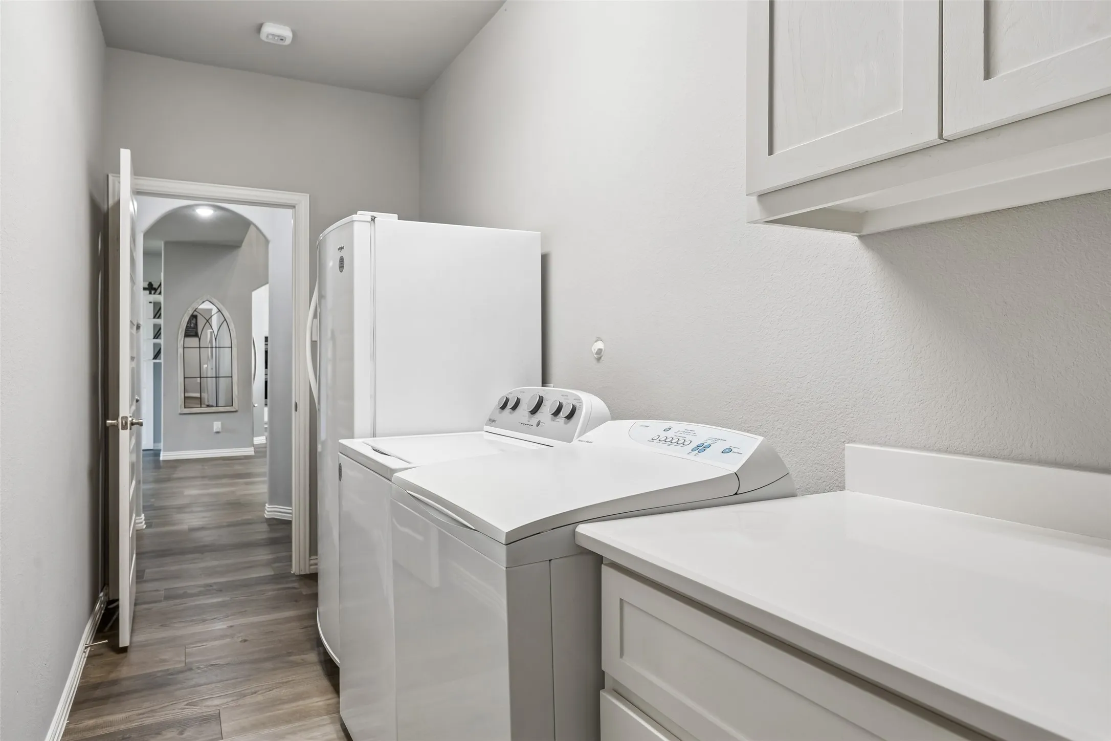 Laundry room with full size washer and dryer, cabinets, countertop and freezer.