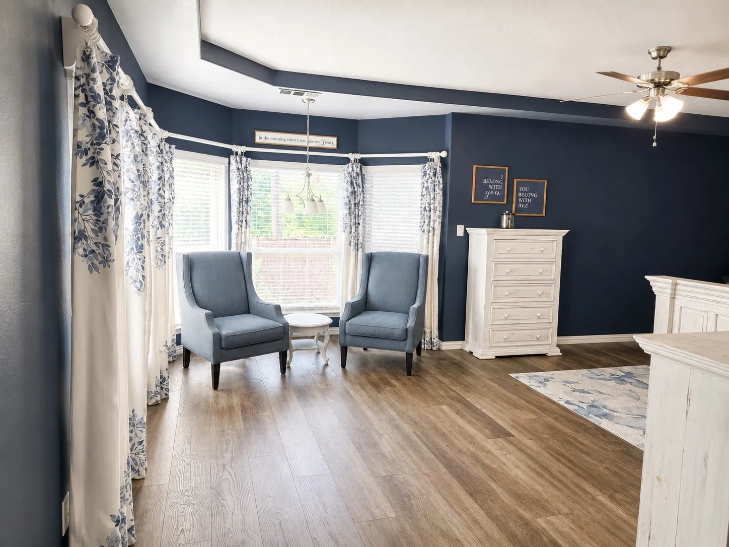 Primary bedroom with a sitting room, LVP flooring, a tray ceiling, ceiling fan and natural light.