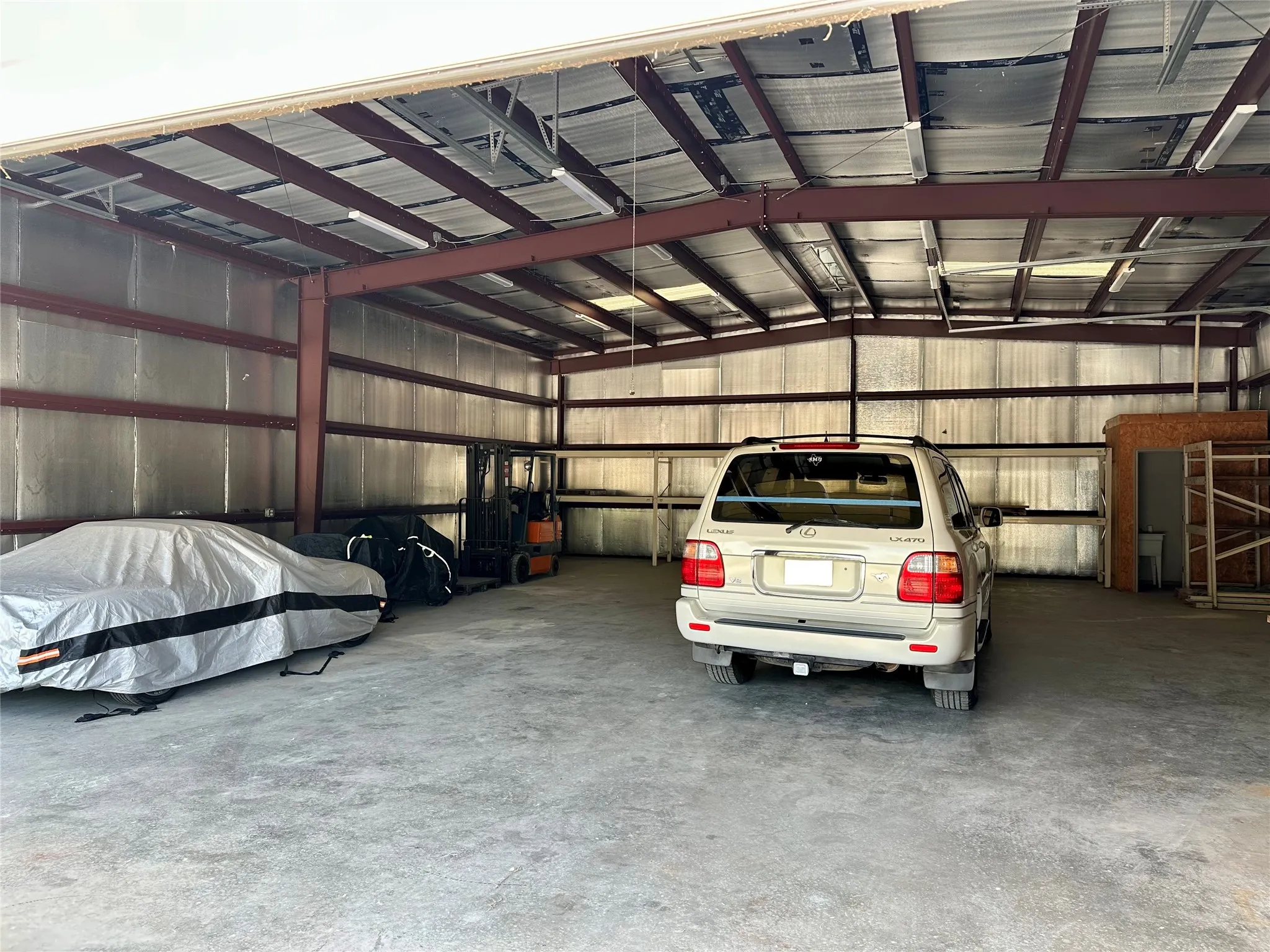 Spacious metal-frame building featuring exposed steel beams, corrugated metal walls, concrete flooring, and fluorescent overhead lighting