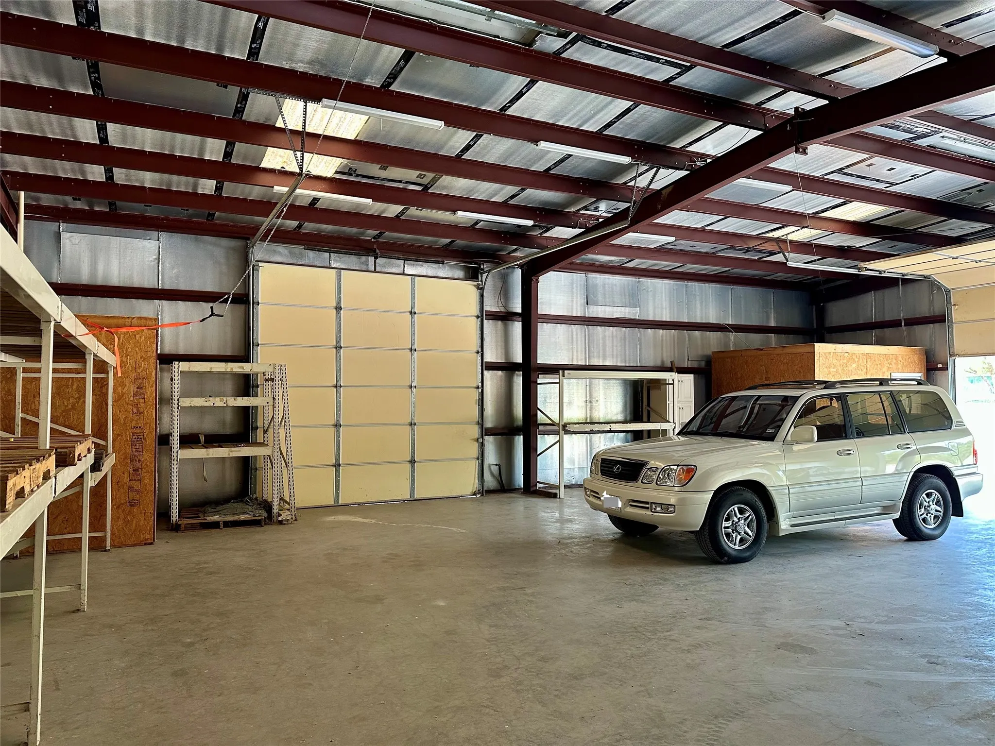 Large garage space featuring a concrete floor, exposed steel beam ceiling, corrugated metal walls, and a large rollup door