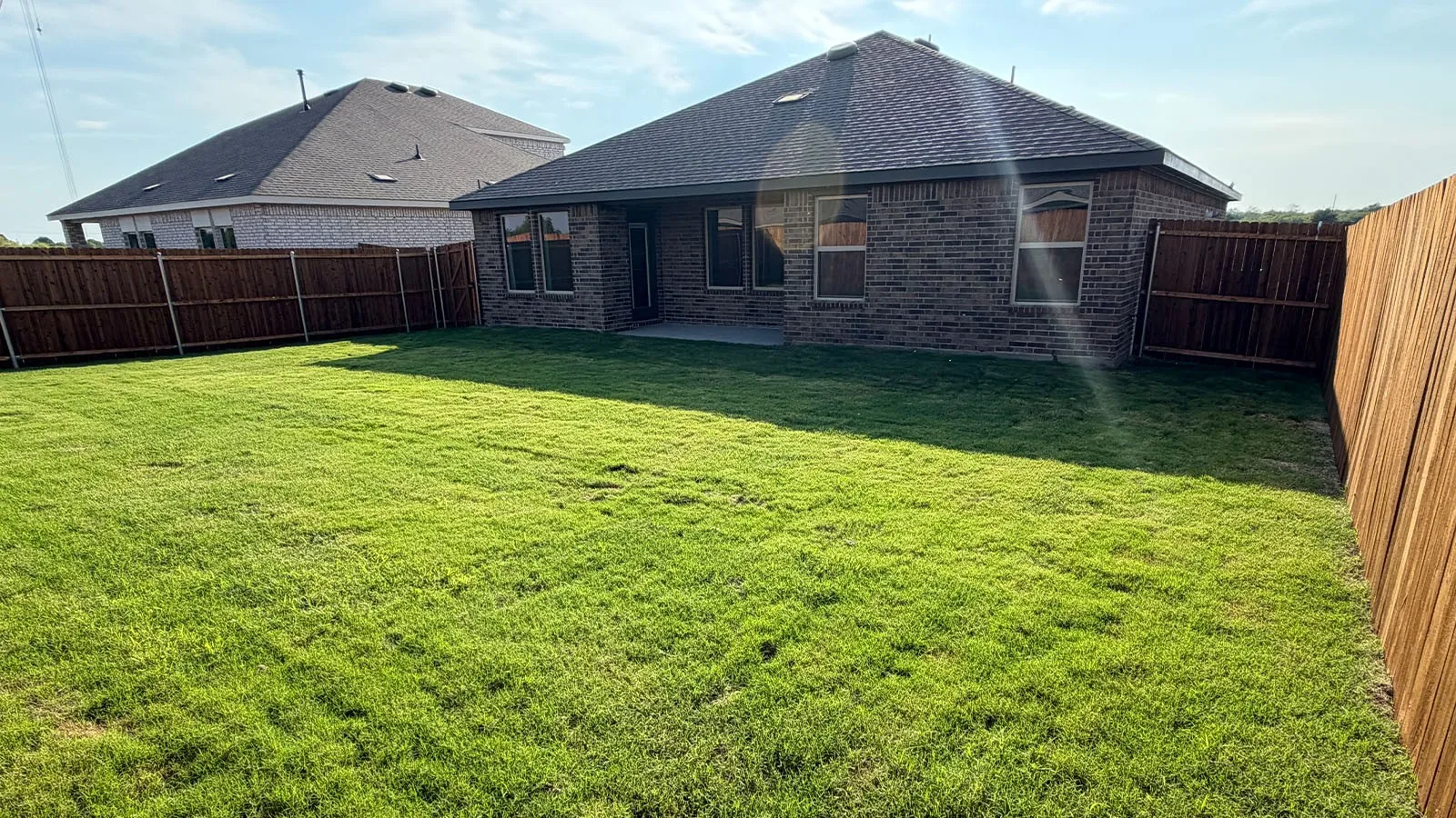 Expansive backyard featuring a manicured lawn, full privacy fencing, and a concrete patio