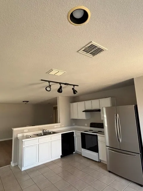 Kitchen featuring white cabinetry, tile flooring, stainless steel refrigerator, black dishwasher, and a black range