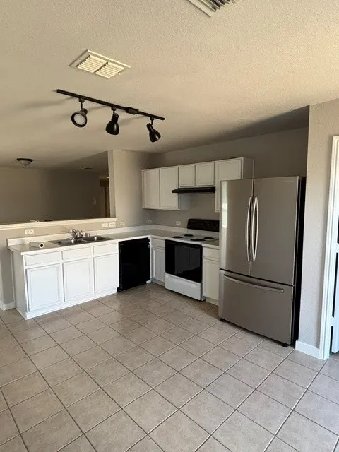 Kitchen featuring white cabinetry, tile flooring, track lighting, stainless steel refrigerator, and integrated sink