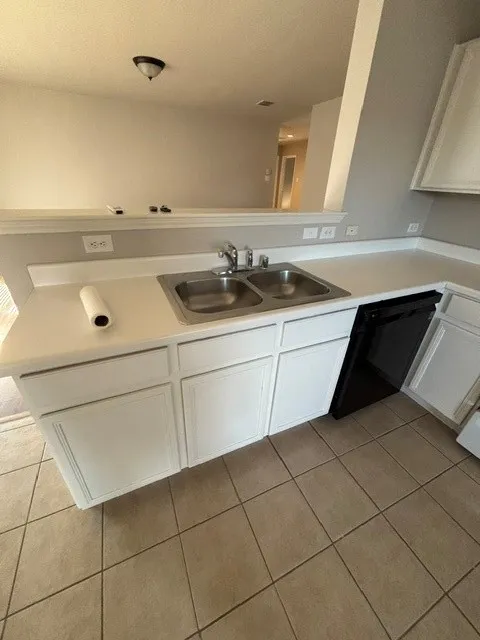 Kitchen featuring white cabinetry, a double basin stainless steel sink, a black dishwasher, and tile flooring