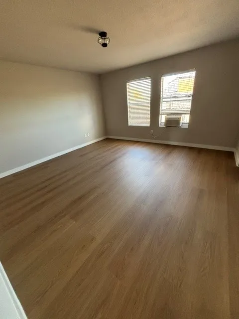 Wood-finish flooring with a neutral wall palette, flush mount lighting, and two windows with horizontal blinds