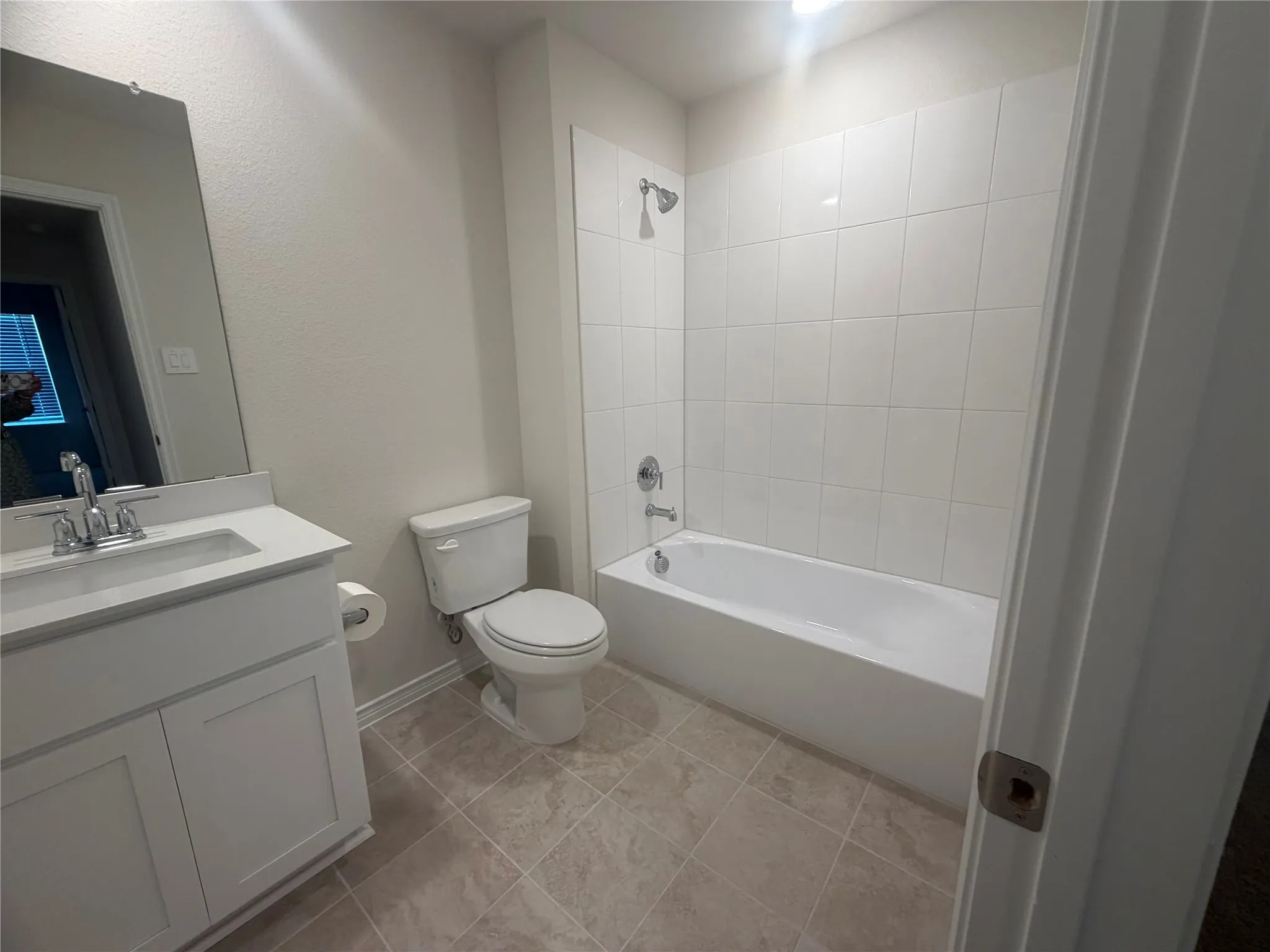 White vanity with an integrated sink, rectangular mirror, full bathtub with a shower, white subway tile surround, and neutral-toned floor tiling