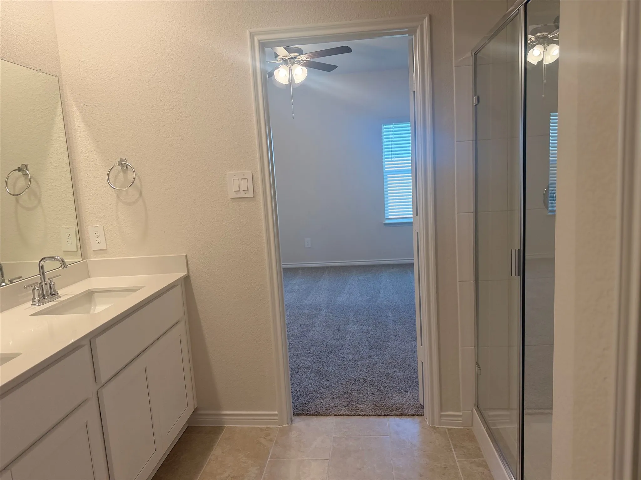 Dual vanity with integrated sinks, a walk-in shower with clear glass enclosure, and tile flooring