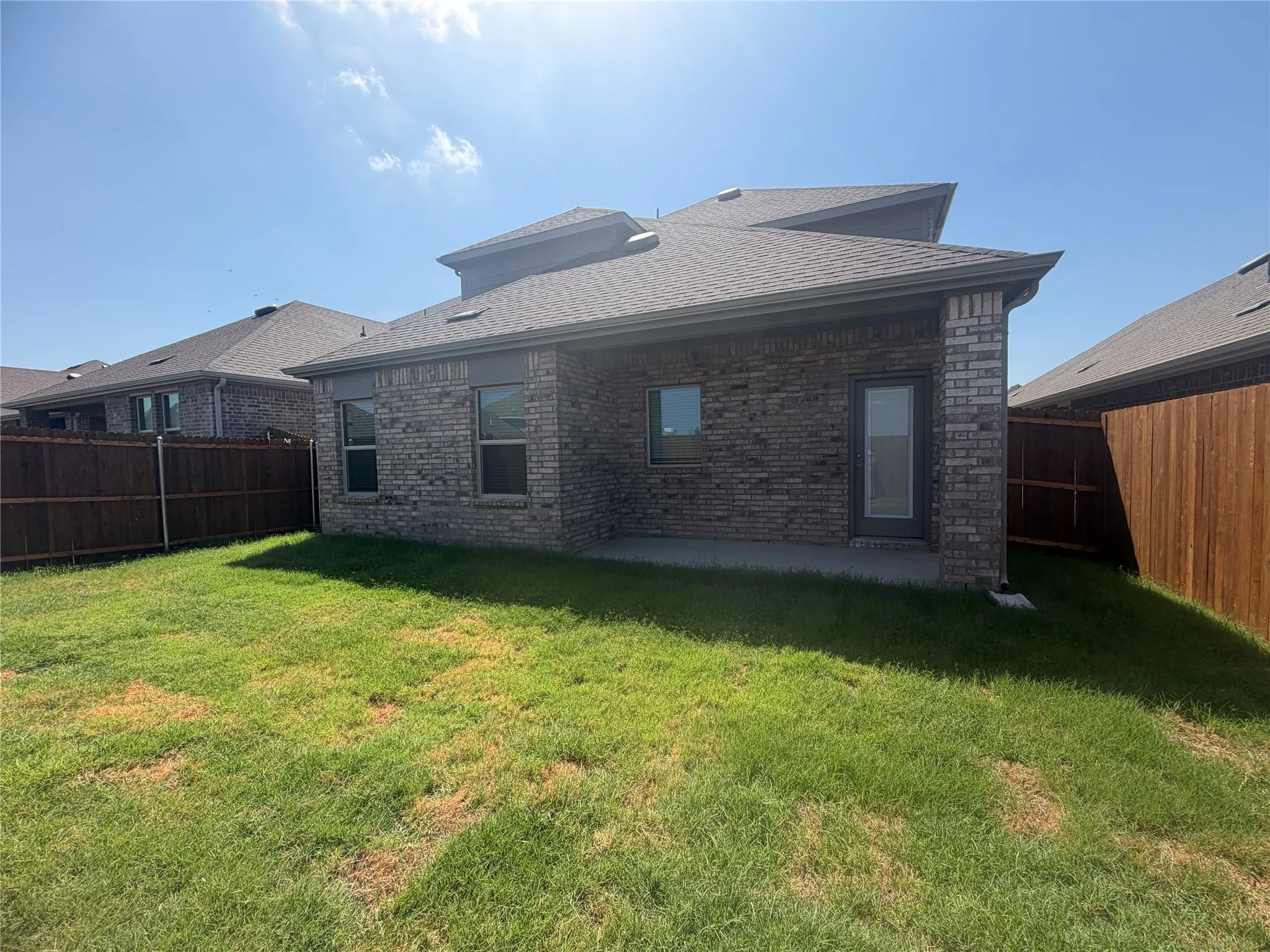 Expansive backyard featuring a manicured lawn, full privacy fencing, a covered patio, and a brick exterior with multiple windows