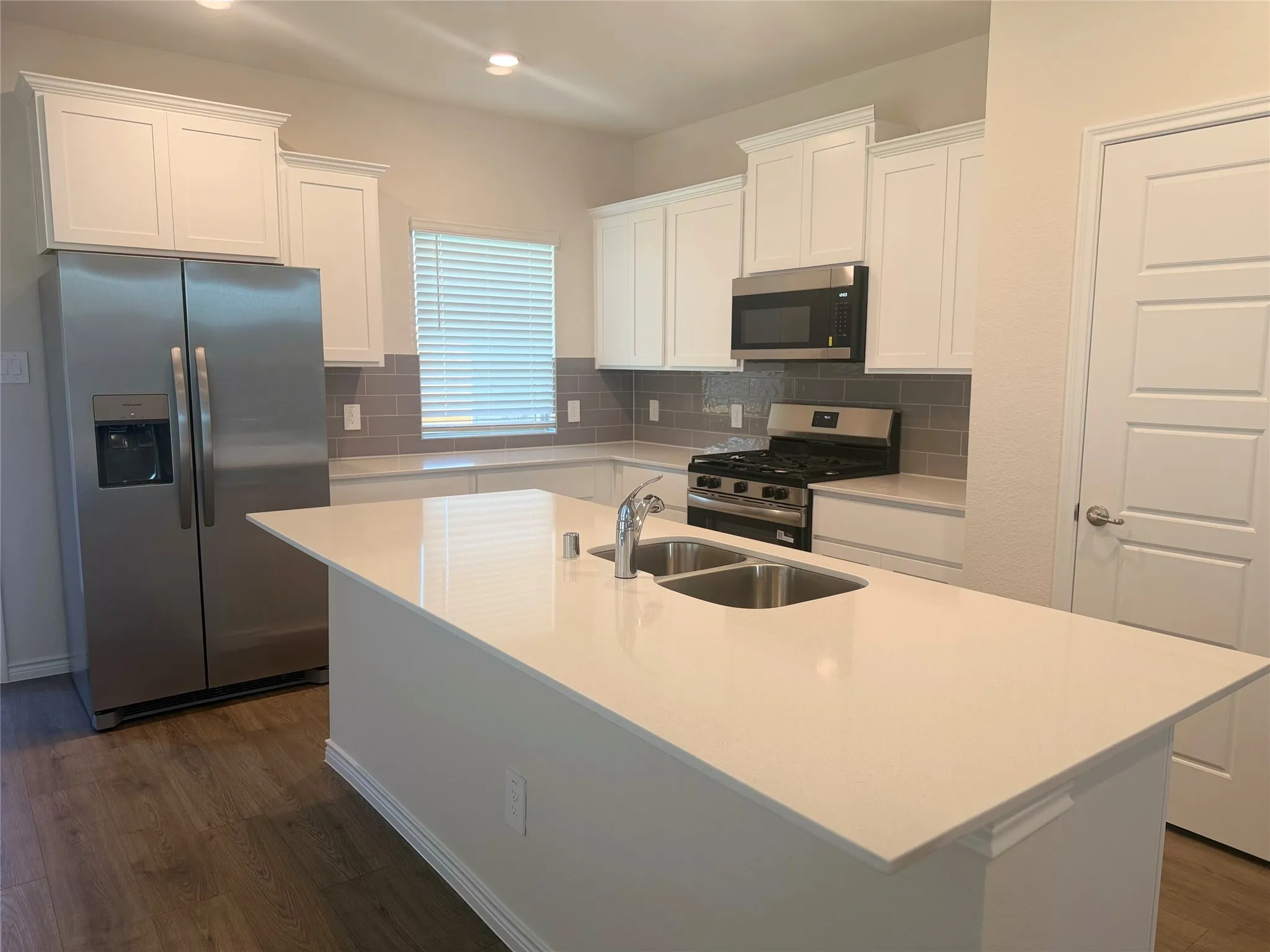 Kitchen featuring an island with an undermount double sink, stainless steel appliances, white cabinetry, and gray subway tile backsplash