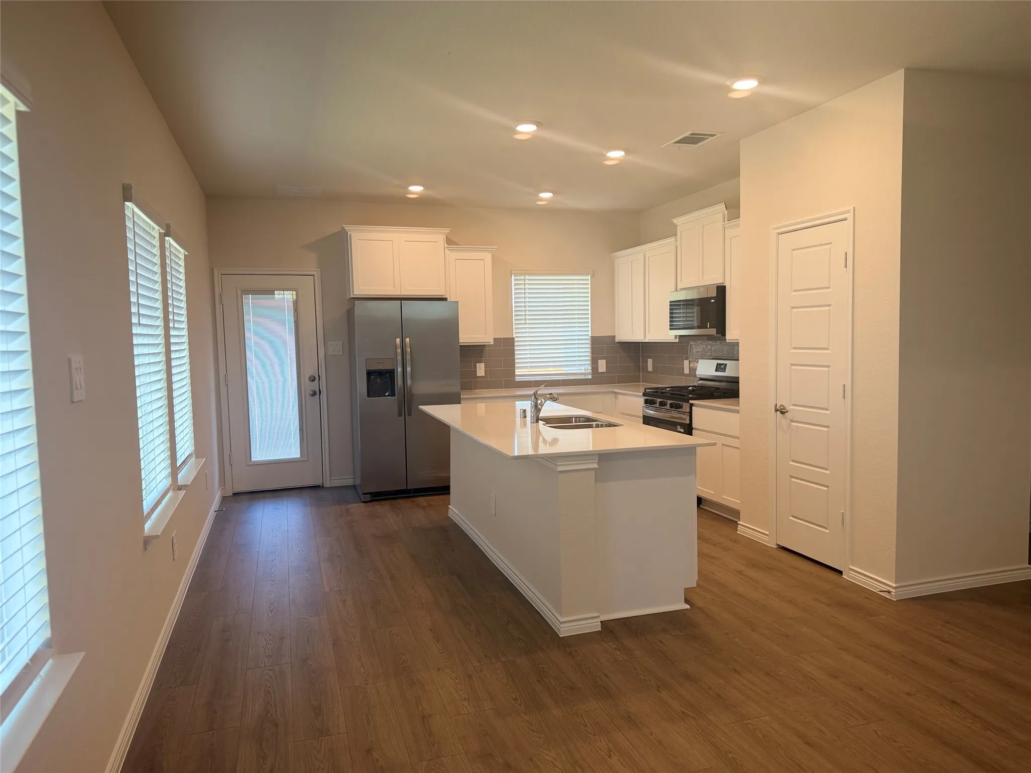 Modern kitchen featuring a central island with a sink, stainless steel appliances, white cabinetry, wood-finish flooring, and recessed lighting