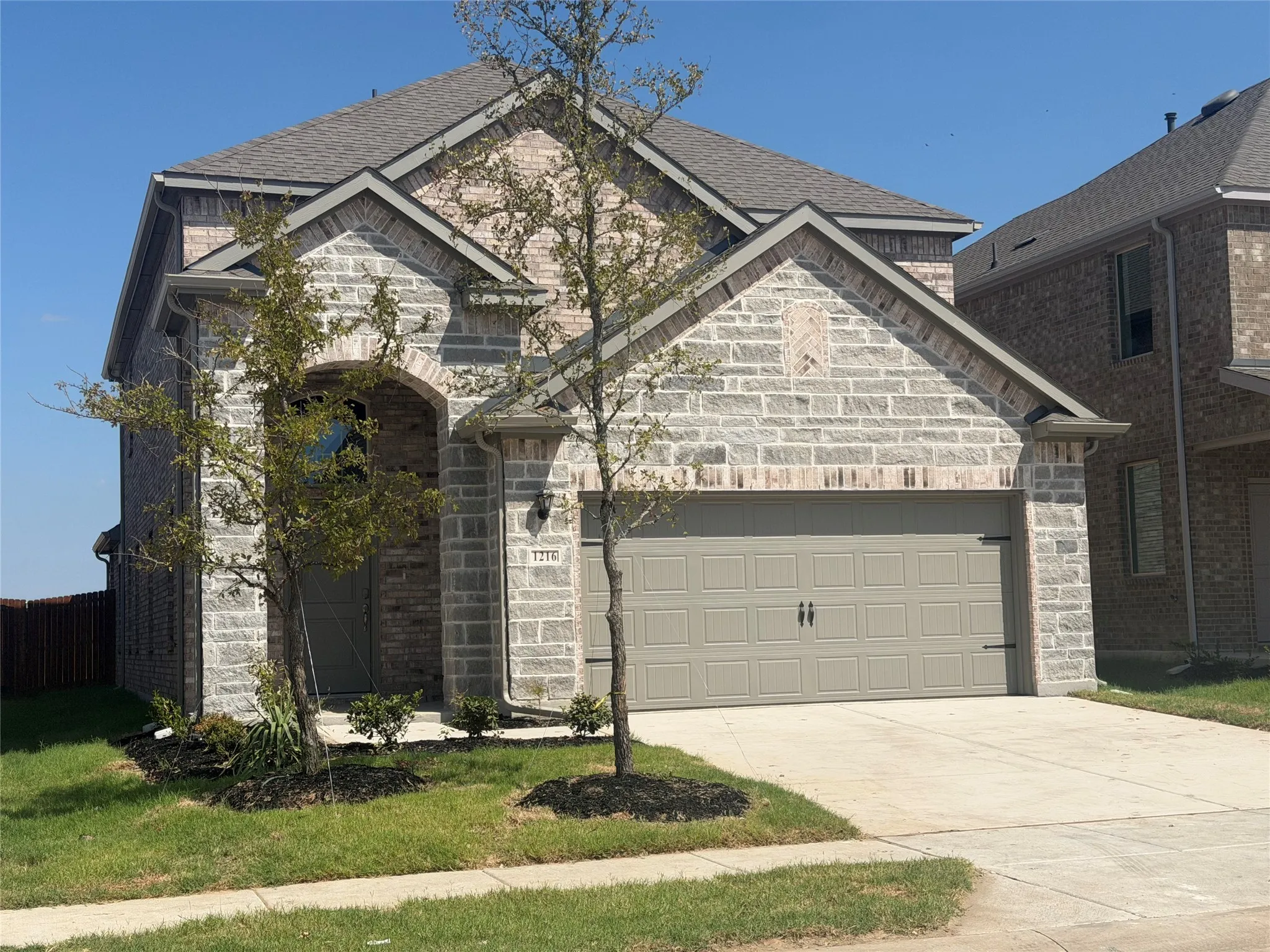 Stone and brick exterior with a paneled garage door, arched entryway, and pitched rooflines