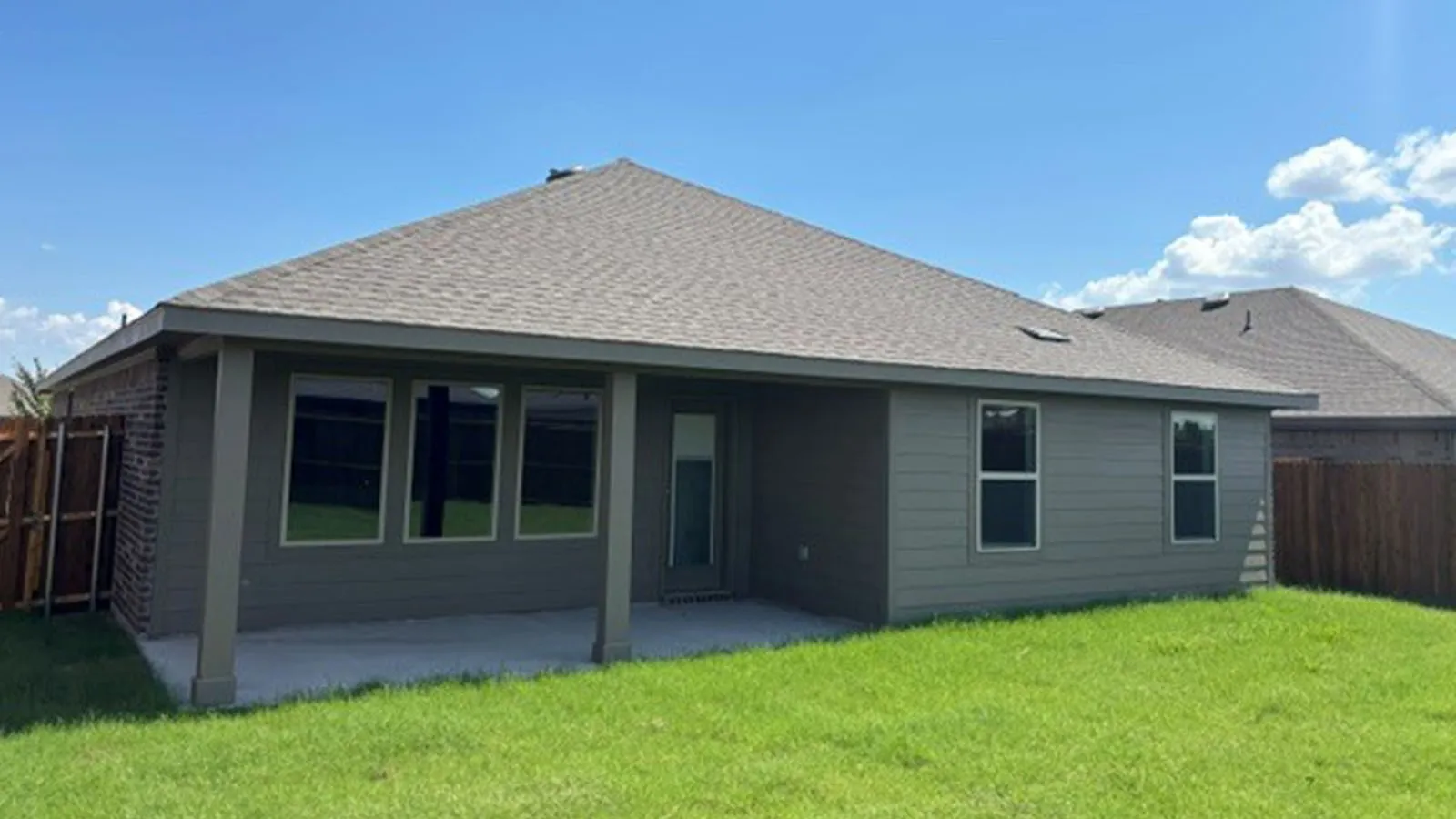 Expansive backyard featuring a covered concrete patio, well-maintained lawn, and a privacy fence