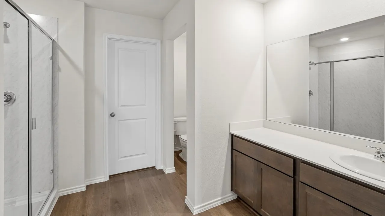 Wood-finish flooring, glass-enclosed shower, expansive vanity with a single sink, white countertop, and dark wood cabinetry