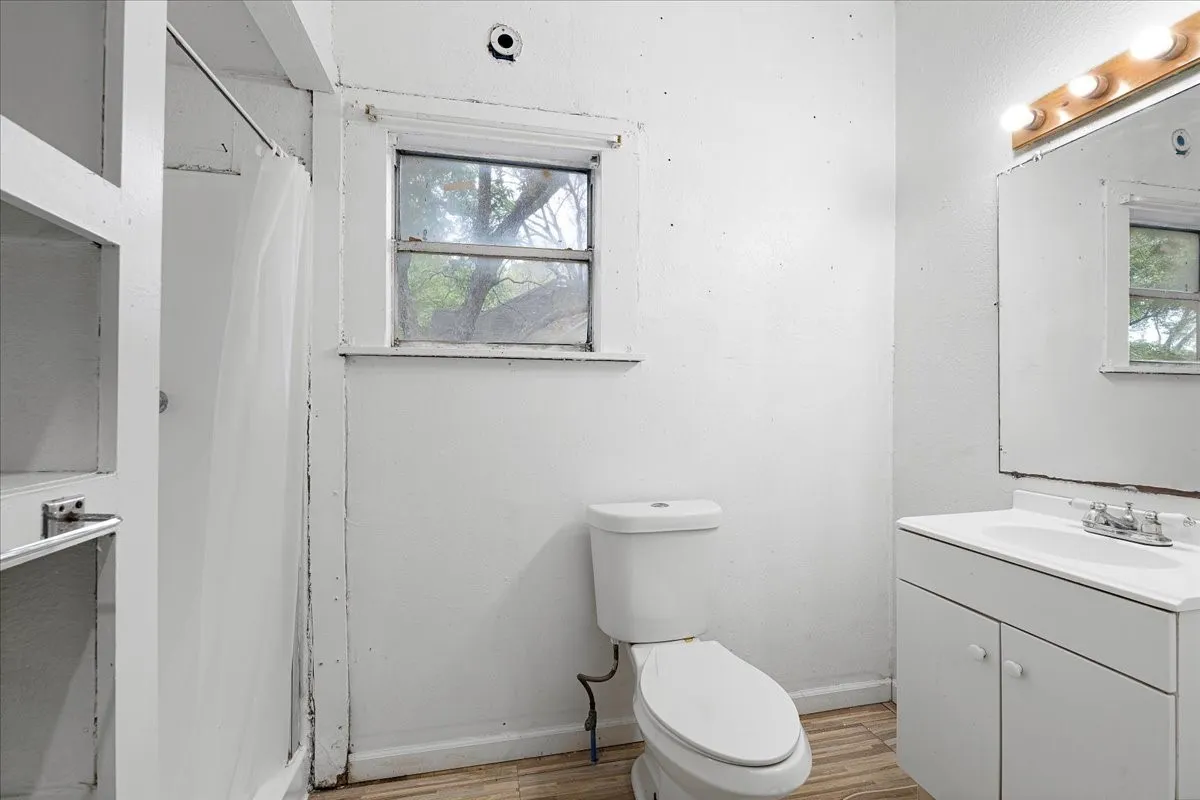White vanity with integrated sink, white toilet, and a window providing natural light