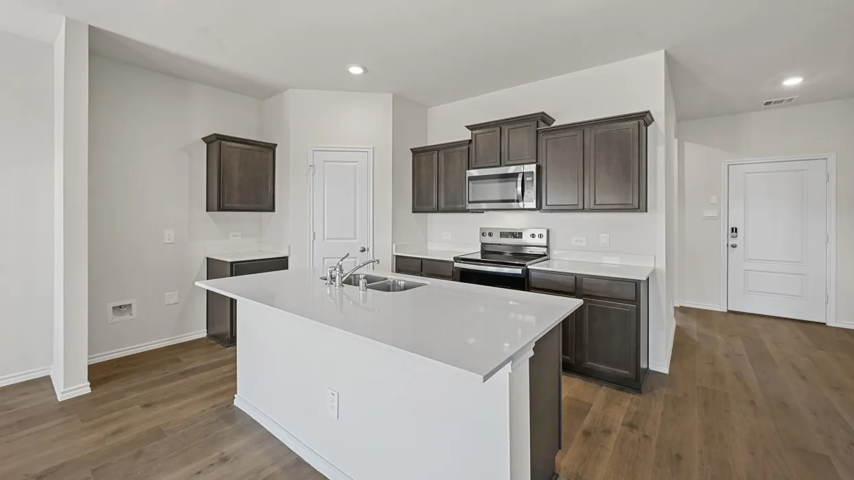 Modern kitchen featuring wood-finish flooring, dark wood cabinetry, stainless steel appliances, a white tile backsplash, and a central island with a double basin sink and white countertop