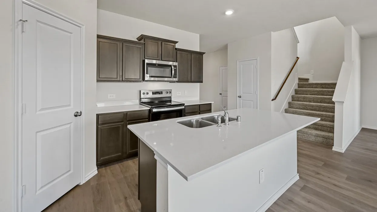 Modern kitchen featuring an island with an undermount double-basin sink, light-toned countertops, dark wood-finish cabinetry, and stainless steel appliances