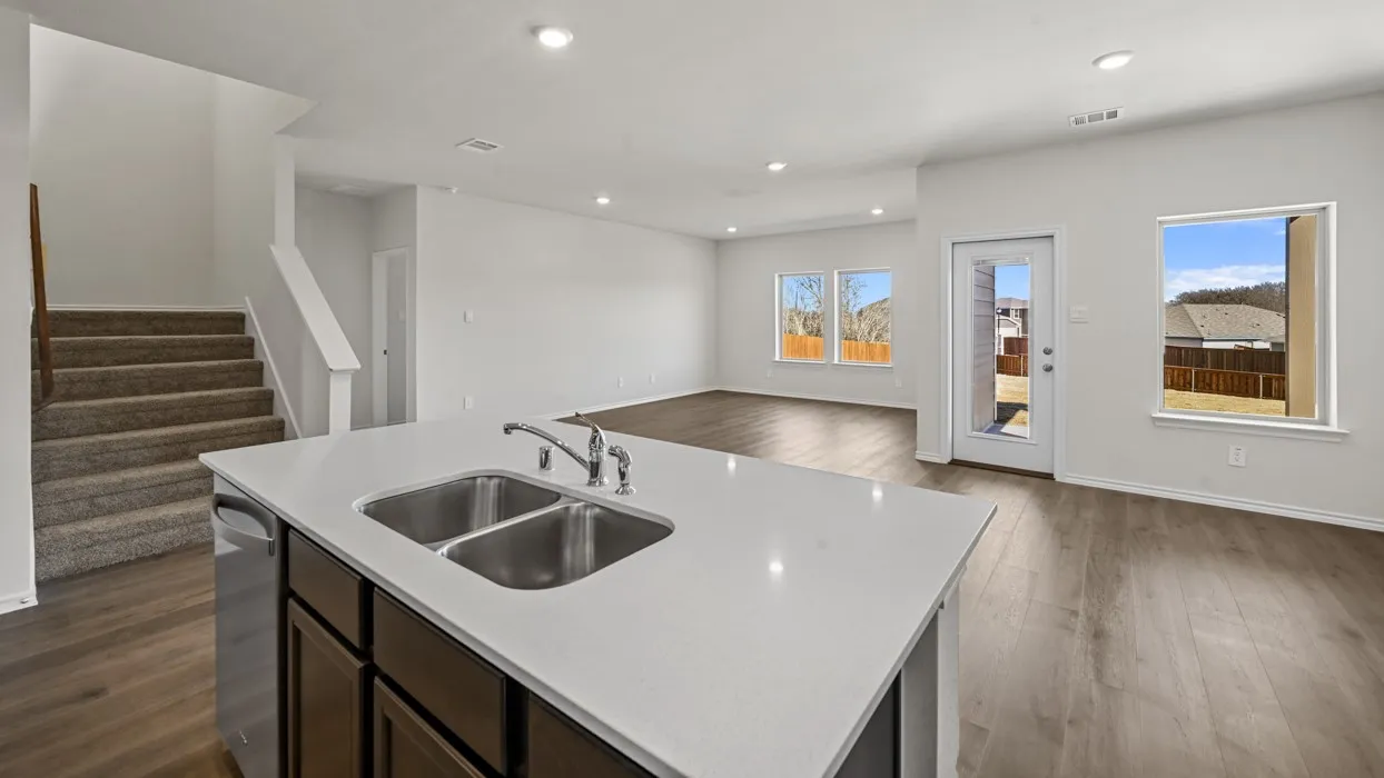 Kitchen island with a double basin sink and a chrome faucet, featuring a light-toned countertop and dark wood-finish cabinetry