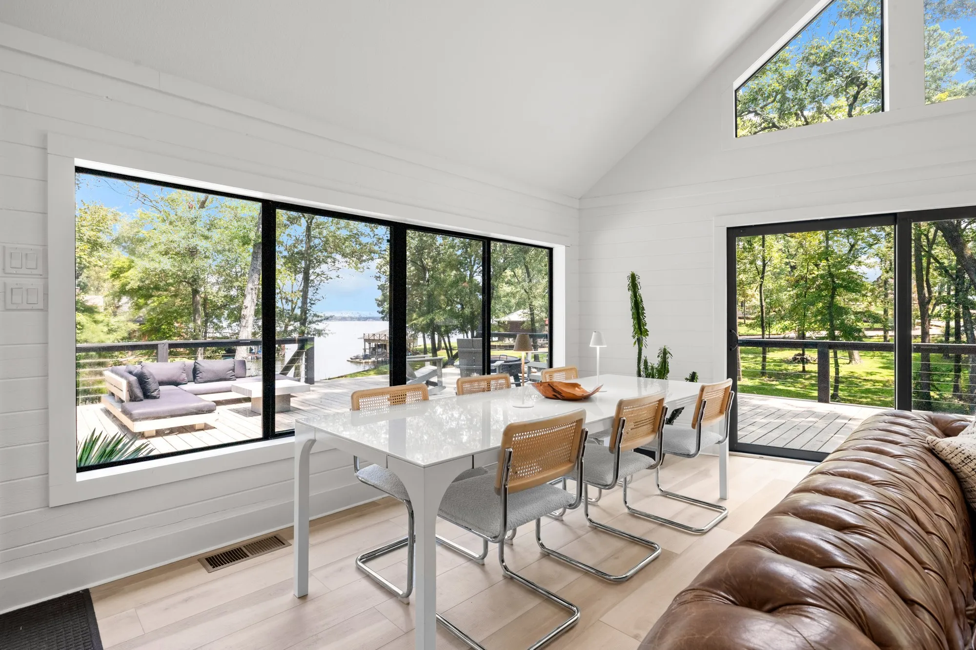 Dining area featuring high vaulted ceiling, plenty of natural light, light wood-type flooring, a water view, and wooden walls