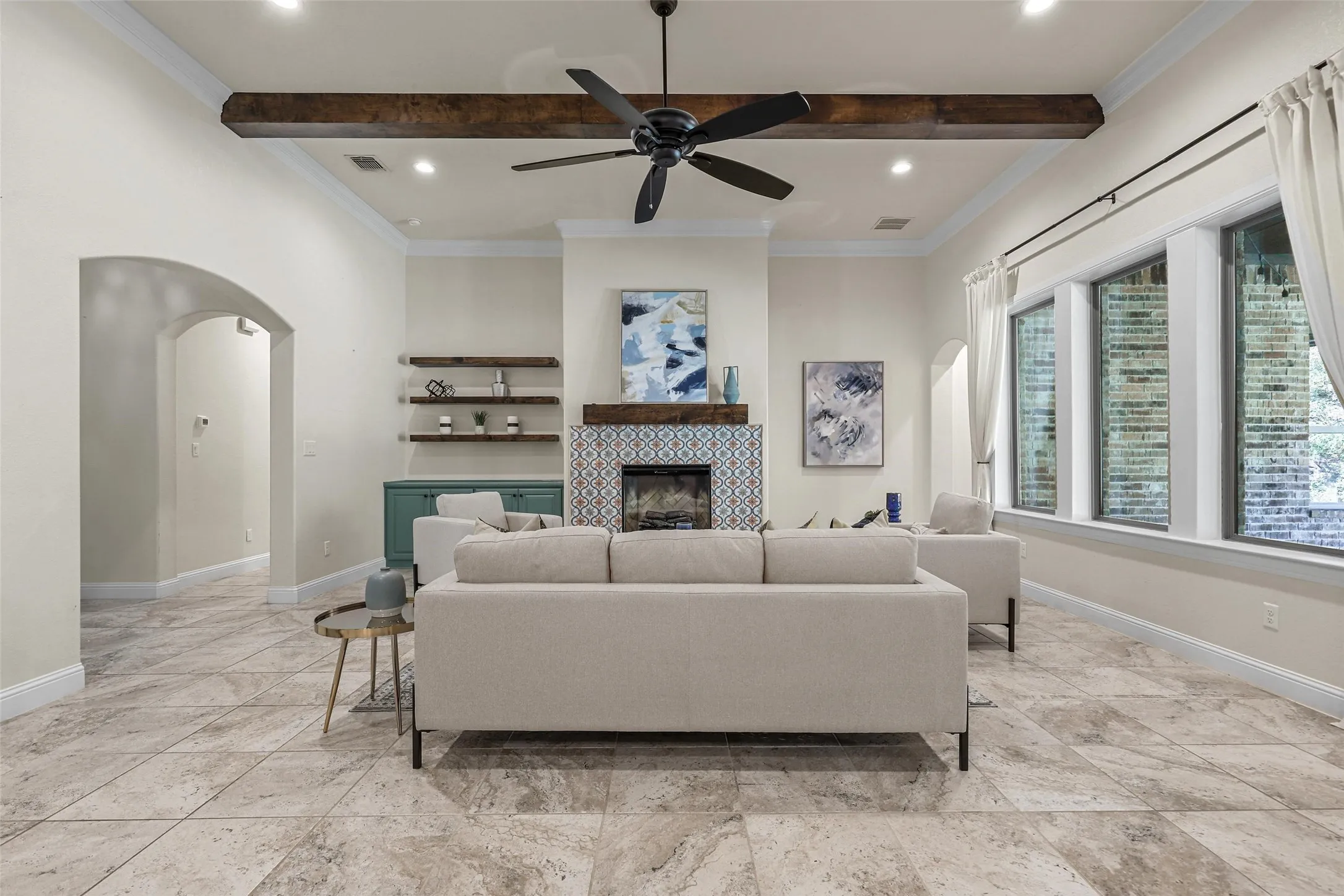 Spacious living area featuring exposed wood beams, a tiled fireplace, recessed lighting, large windows, and a ceiling fan
