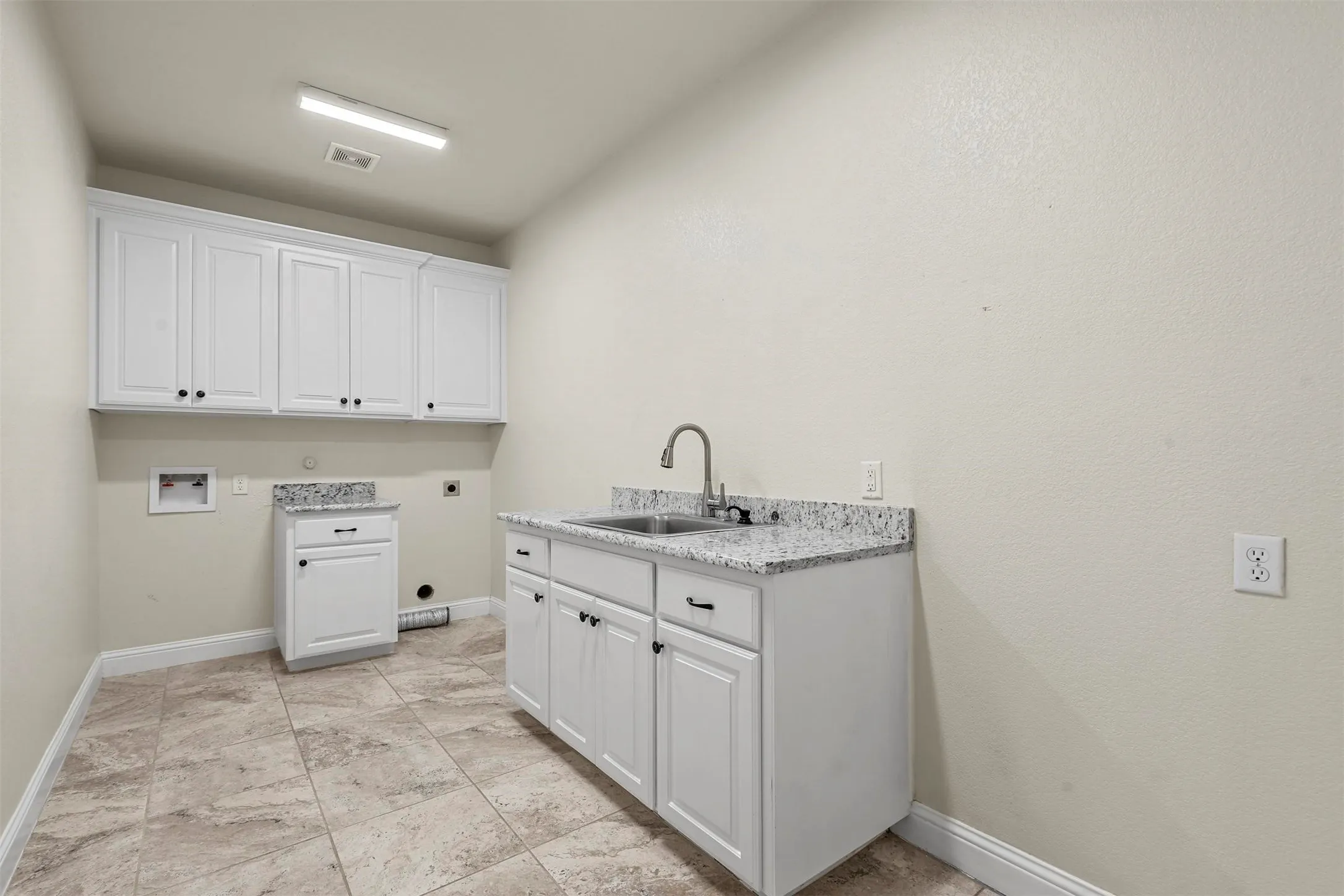 Laundry area with extensive white cabinetry, a utility sink, light-toned tiled flooring, and granite countertops