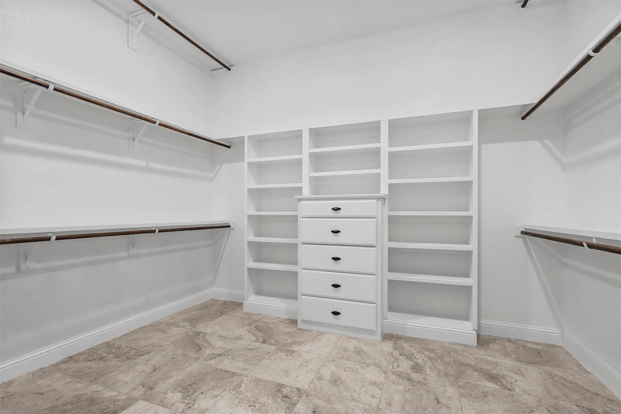 Expansive walk-in closet featuring built-in shelving, integrated drawer storage, dual hanging rods, and tile flooring