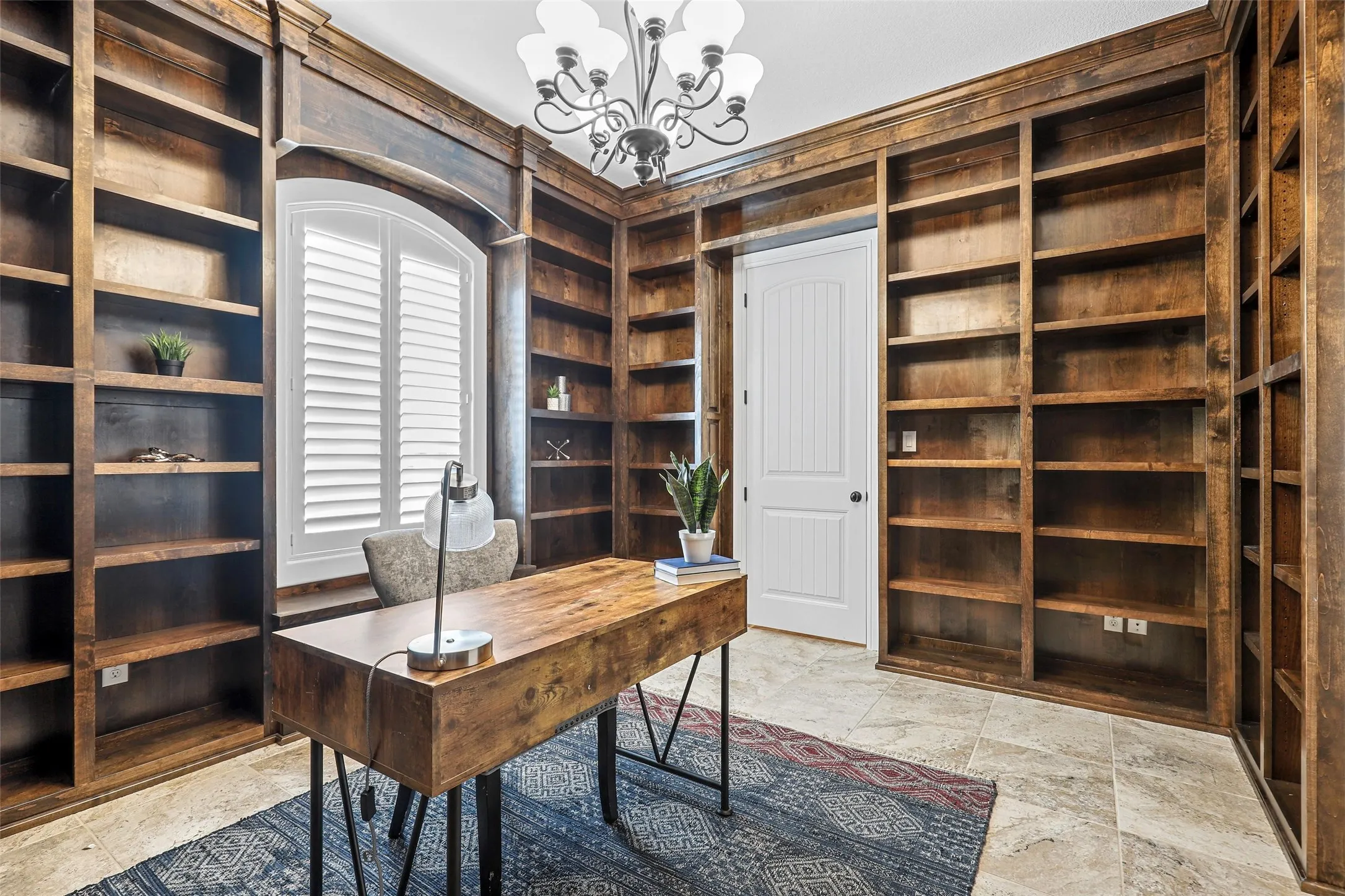 Built-in wood shelving, arched window with plantation shutters, tile flooring, and a white paneled door