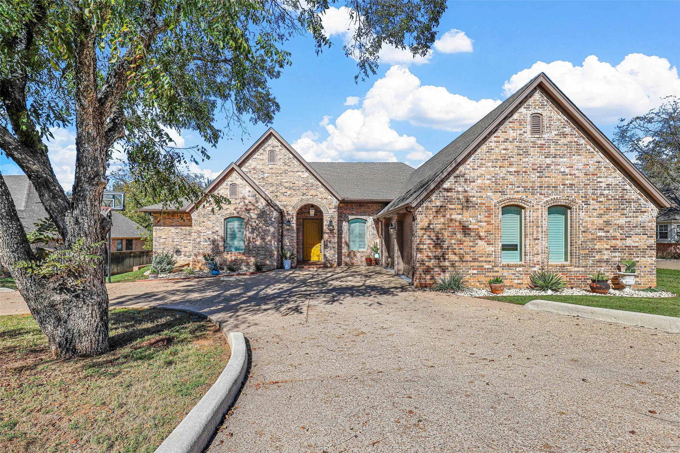 Brick exterior with gabled roofs, arched entry, and a gravel driveway