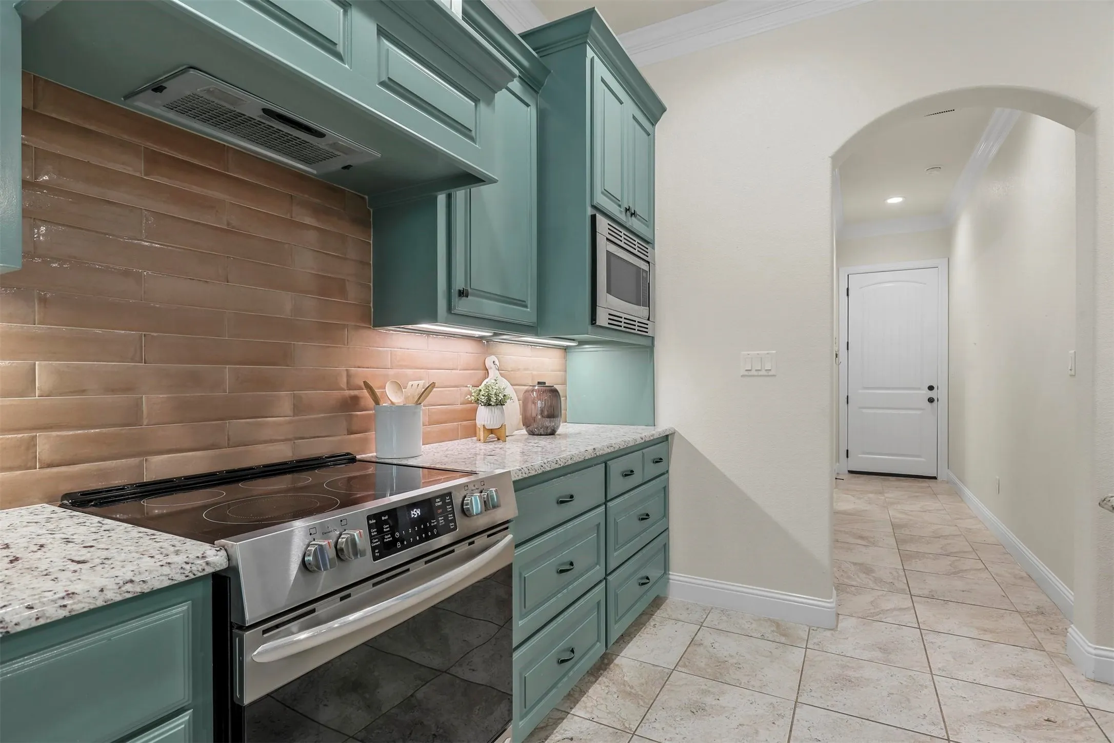 Stainless steel range with a flat cooktop, under-cabinet microwave, teal cabinetry, light granite countertops, and light rectangular backsplash tiles