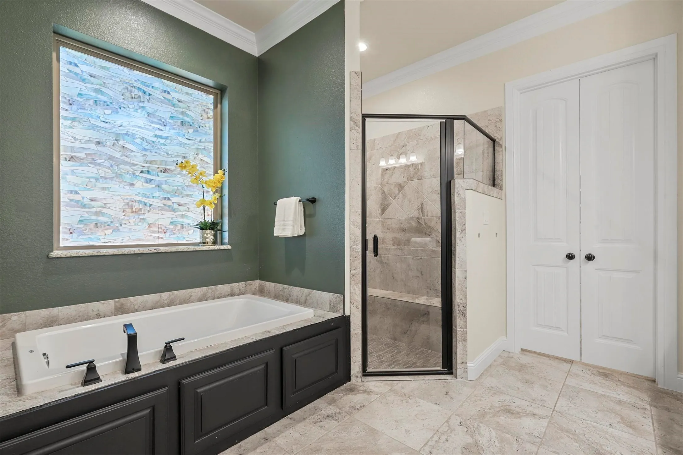 Built-in soaking tub with dark-finish cabinetry, a large privacy window, and a separate shower with a glass enclosure