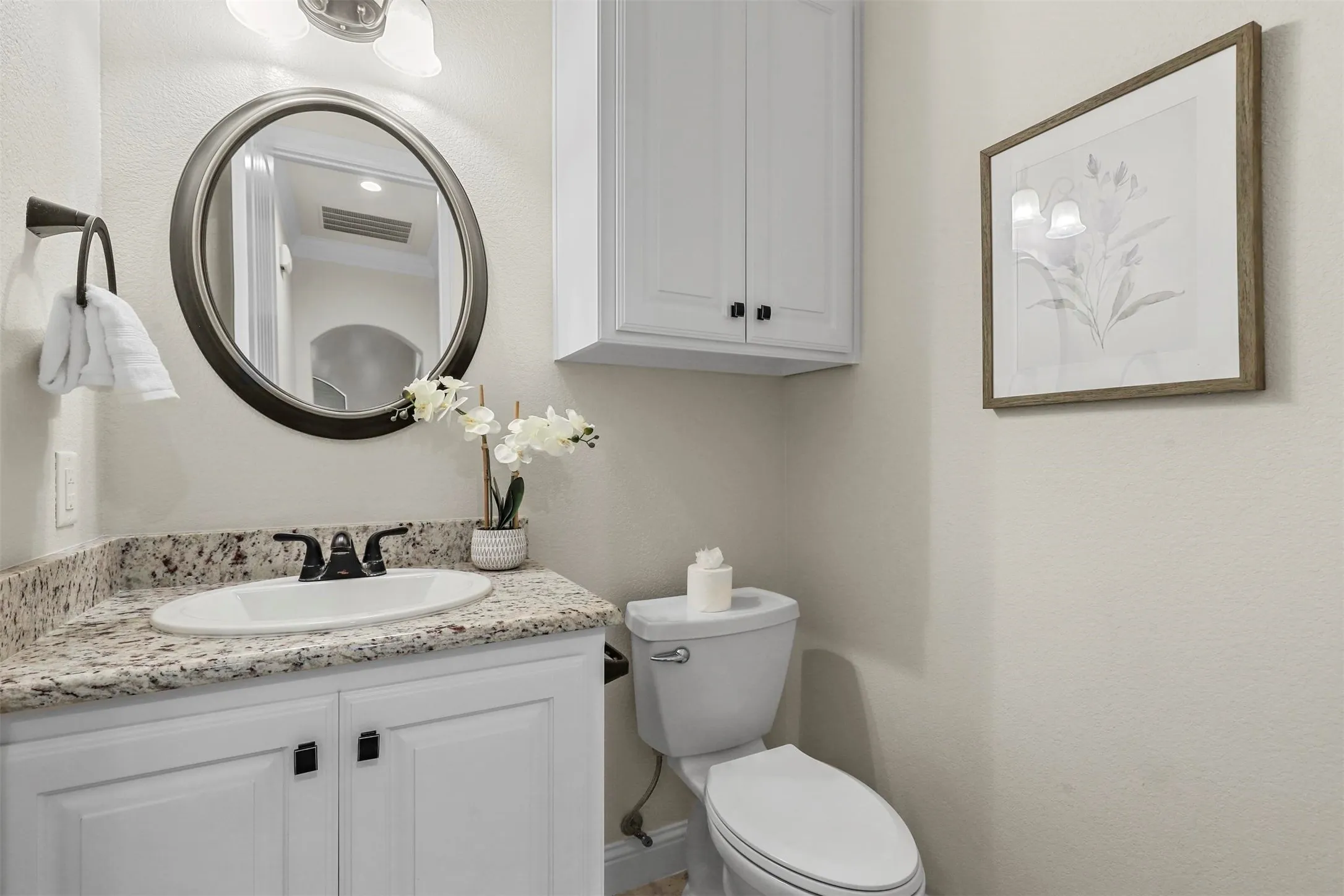 White vanity with black hardware, an oval undermount sink, and a speckled countertop