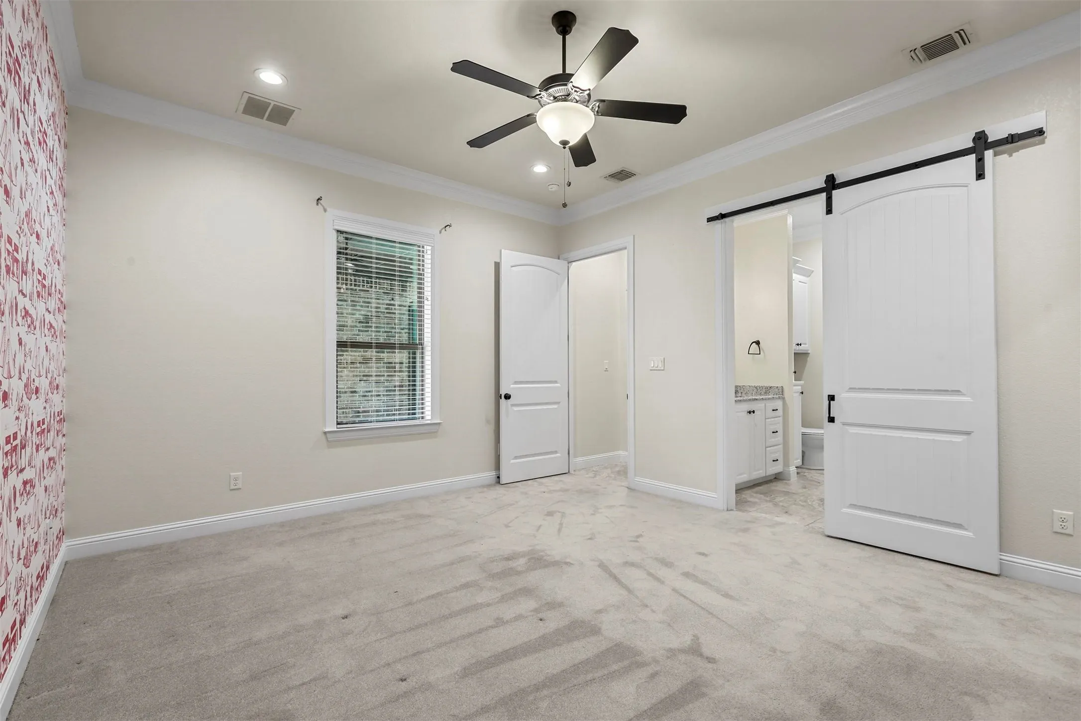 Ceiling fan with integrated lighting, recessed lighting, crown molding, white trim, and a barn door leading to an en-suite with a vanity featuring a stone countertop