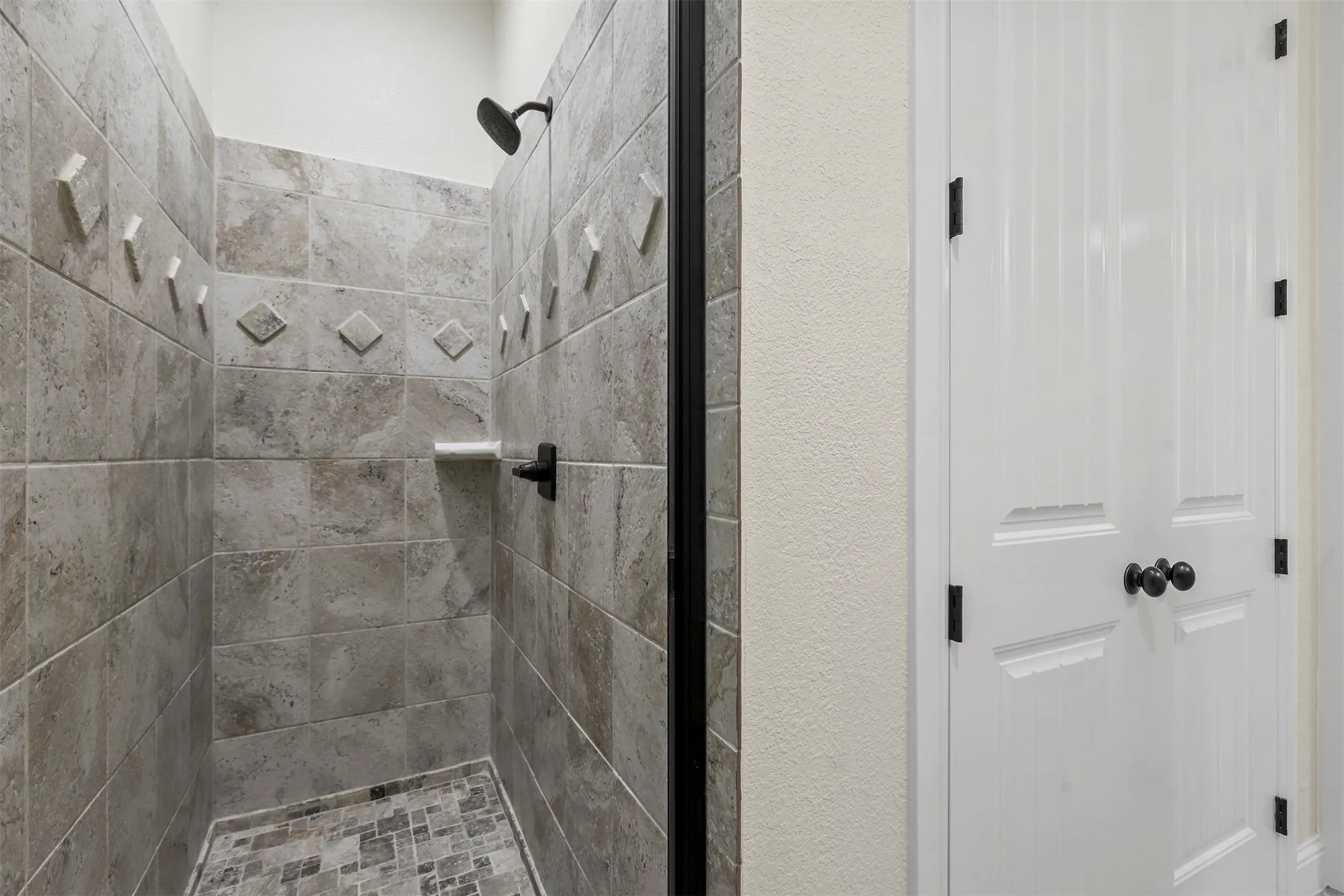 Tiled shower with a textured accent band, integrated shelf, and matte black fixtures