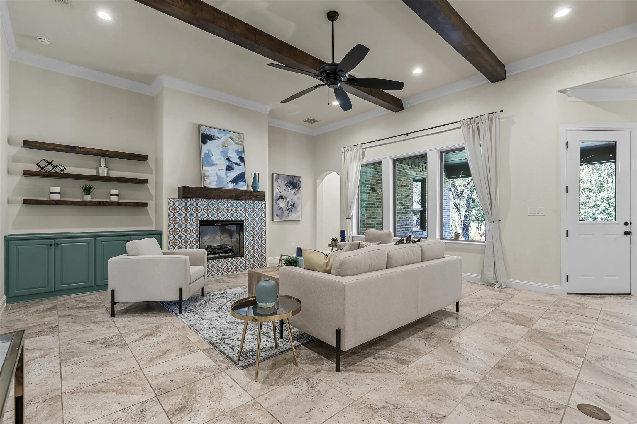 Living area featuring tile flooring, exposed wood beams, a fireplace with decorative tile surround, built-in shelving, and a ceiling fan